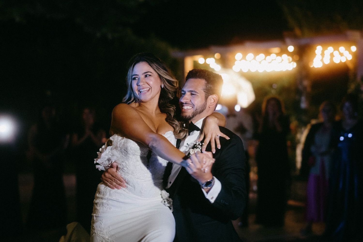 Couple dances together at a dimly lit wedding reception with twinkling lights in the background.