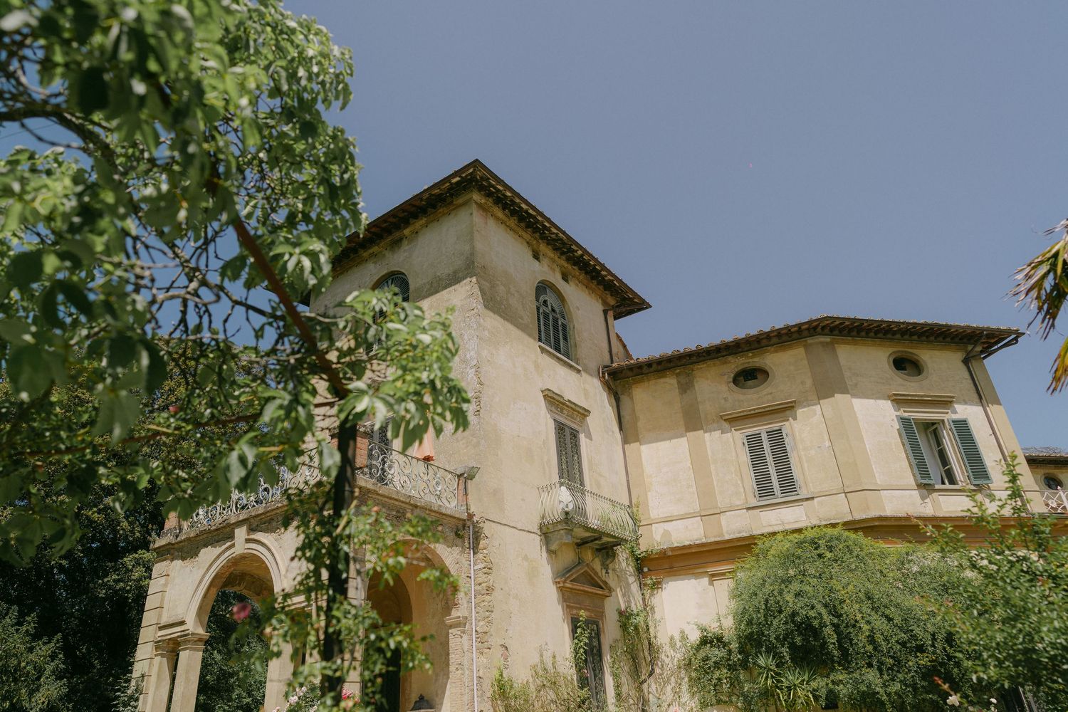 Mediterranean villa with stone walls and green foliage surrounds the exterior architecture in summer sunlight.