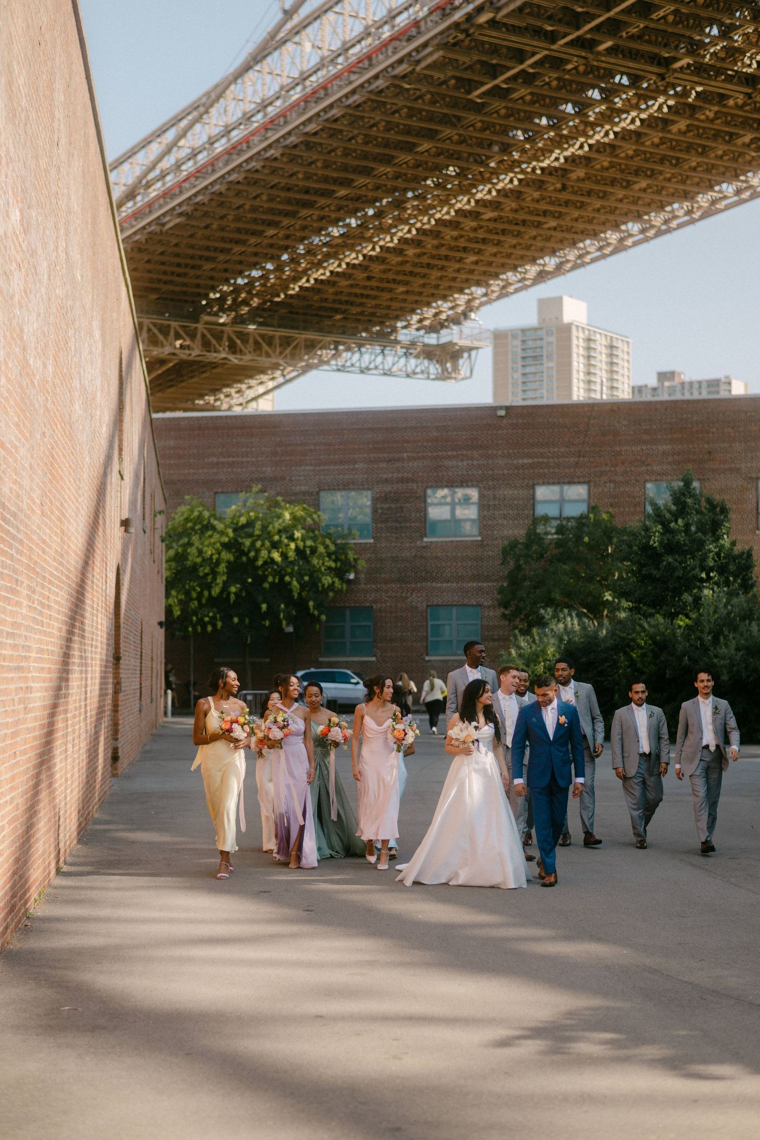 Wedding party gathers under a modern architectural structure with exposed beams and natural lighting.