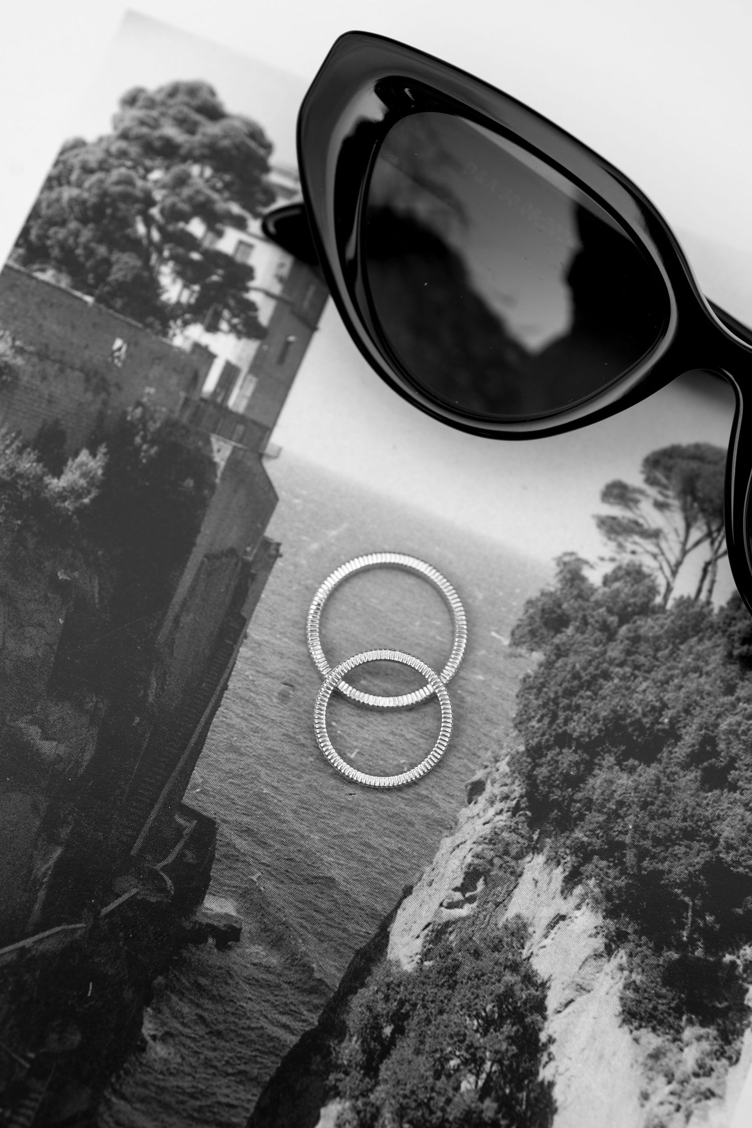 A series of black and white photographs showing sunglasses and wedding rings against various outdoor backgrounds.