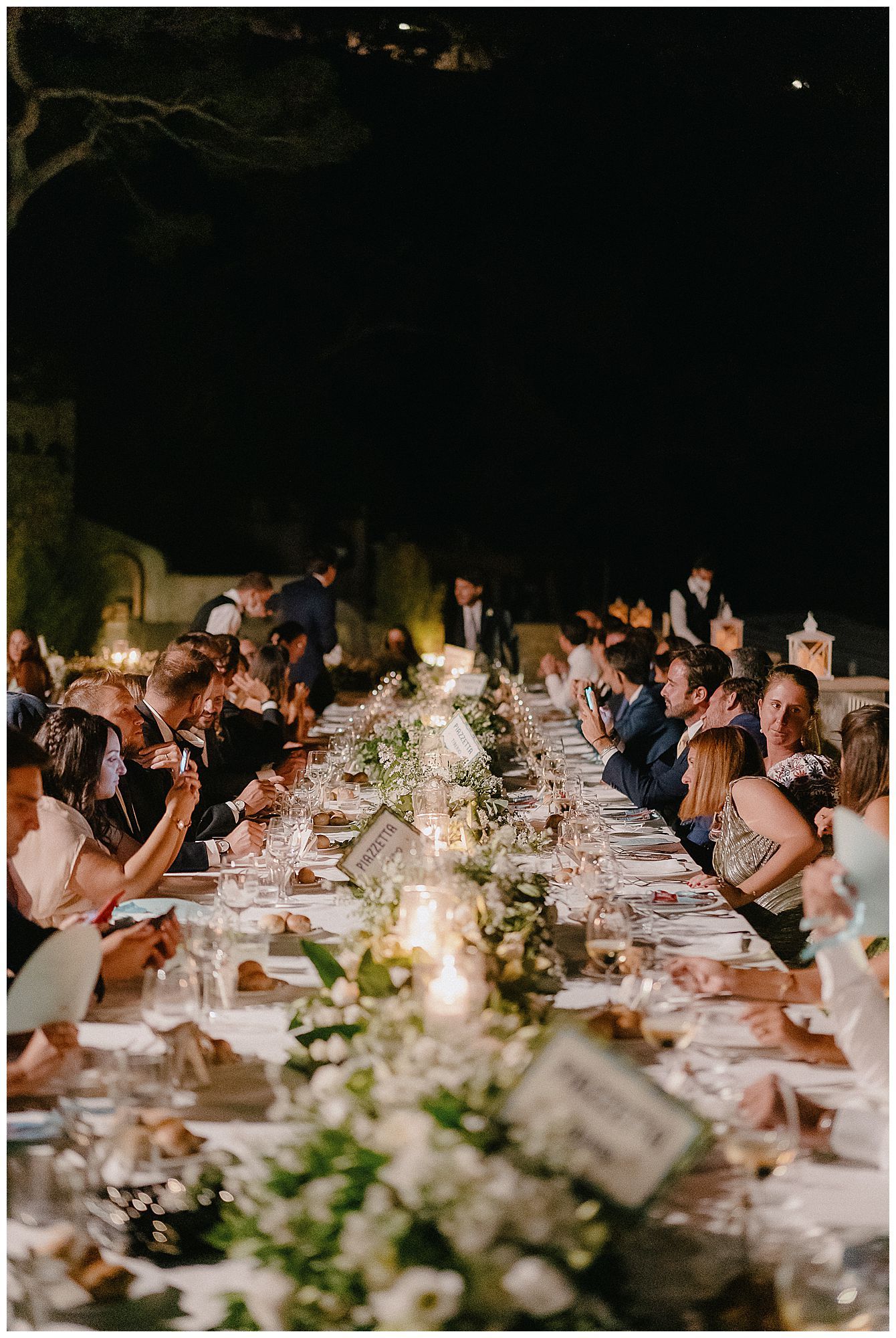 Elegant wedding reception dinner table decorated with candlelight and greenery garlands in a dimly lit venue.