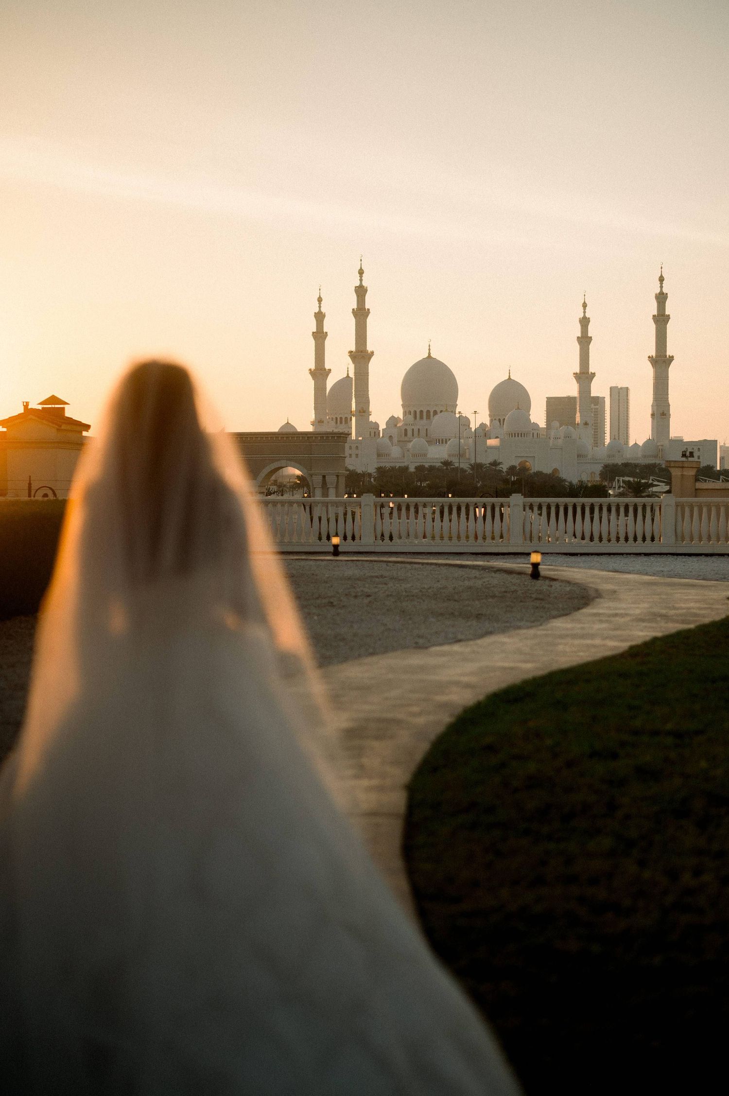 Silhouette of Sheikh Zayed Grand Mosque at sunset with figure in white dress viewing from terrace in Abu Dhabi.