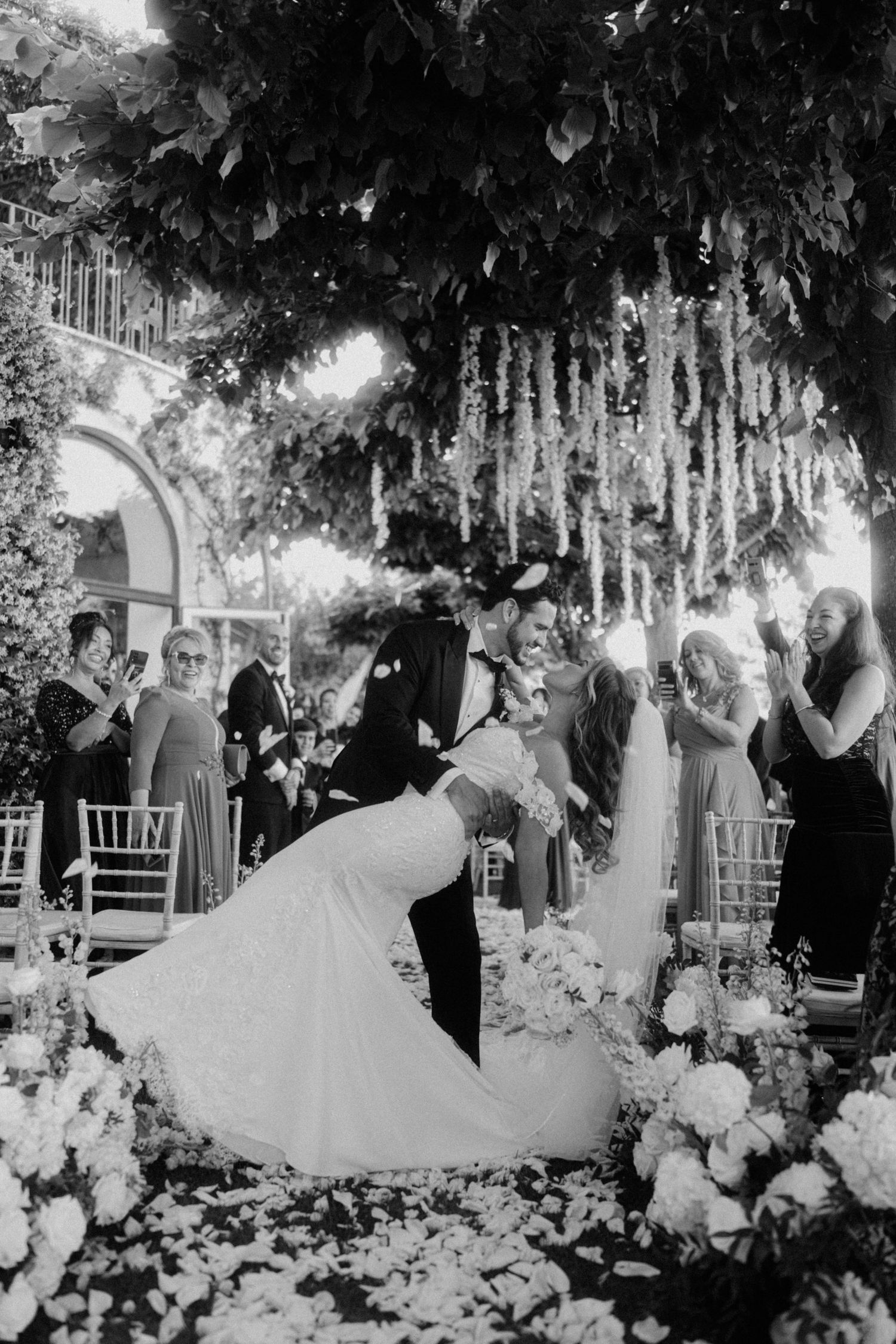 A sequence of black and white wedding photos showing a couple dancing among floral decorations at an outdoor reception.