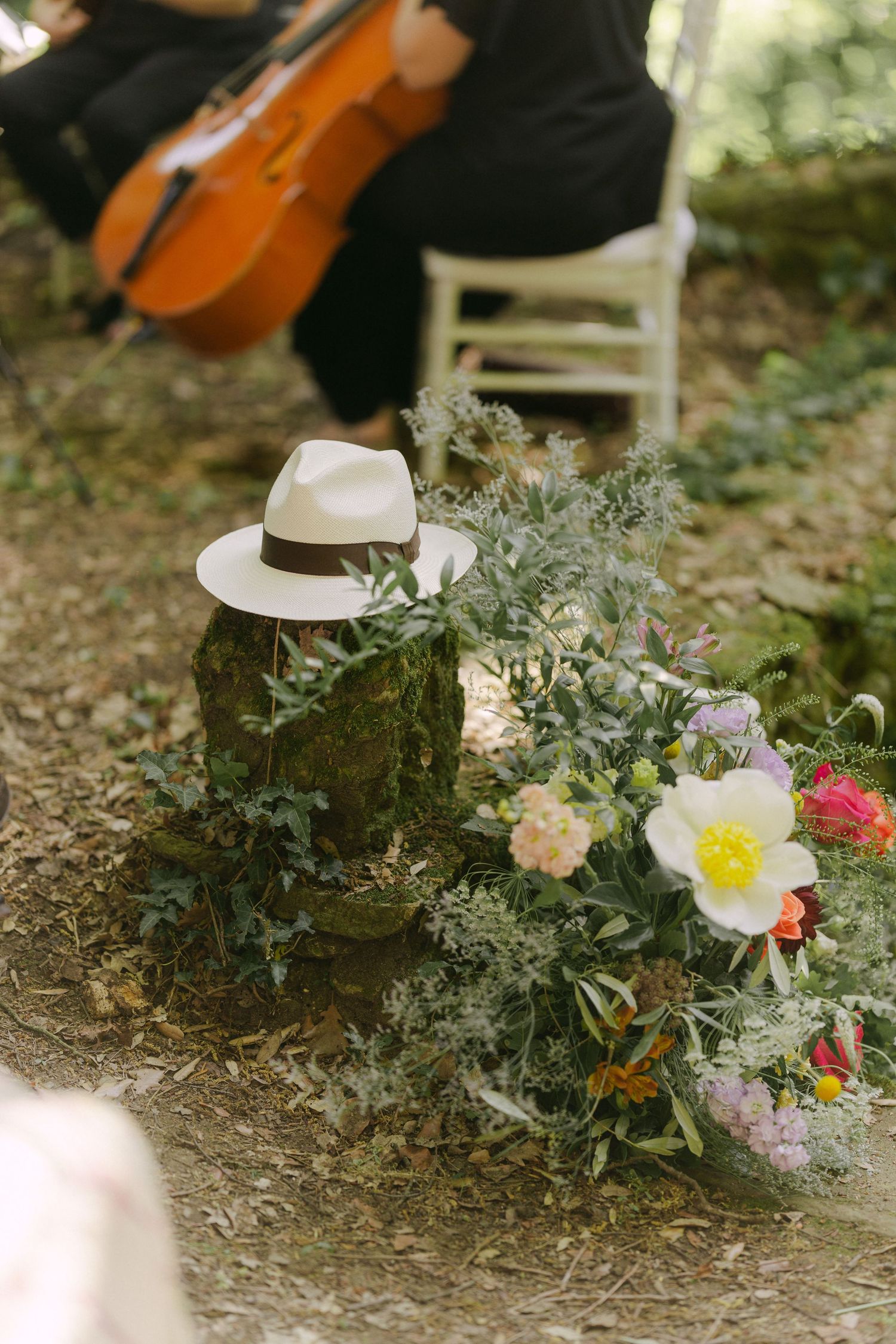 Elegant outdoor wedding decor features violins, white hats, and delicate floral arrangements on natural ground.