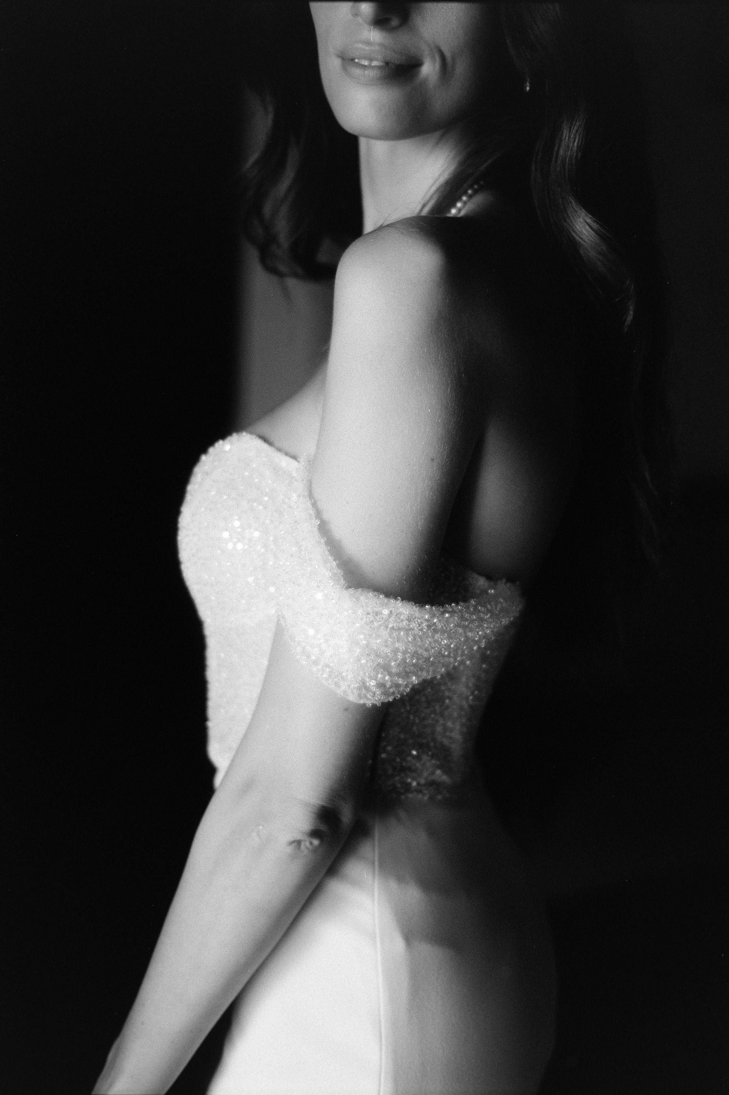 Black and white close-up of a bride in a strapless beaded wedding dress showing elegant silhouette against dark background.