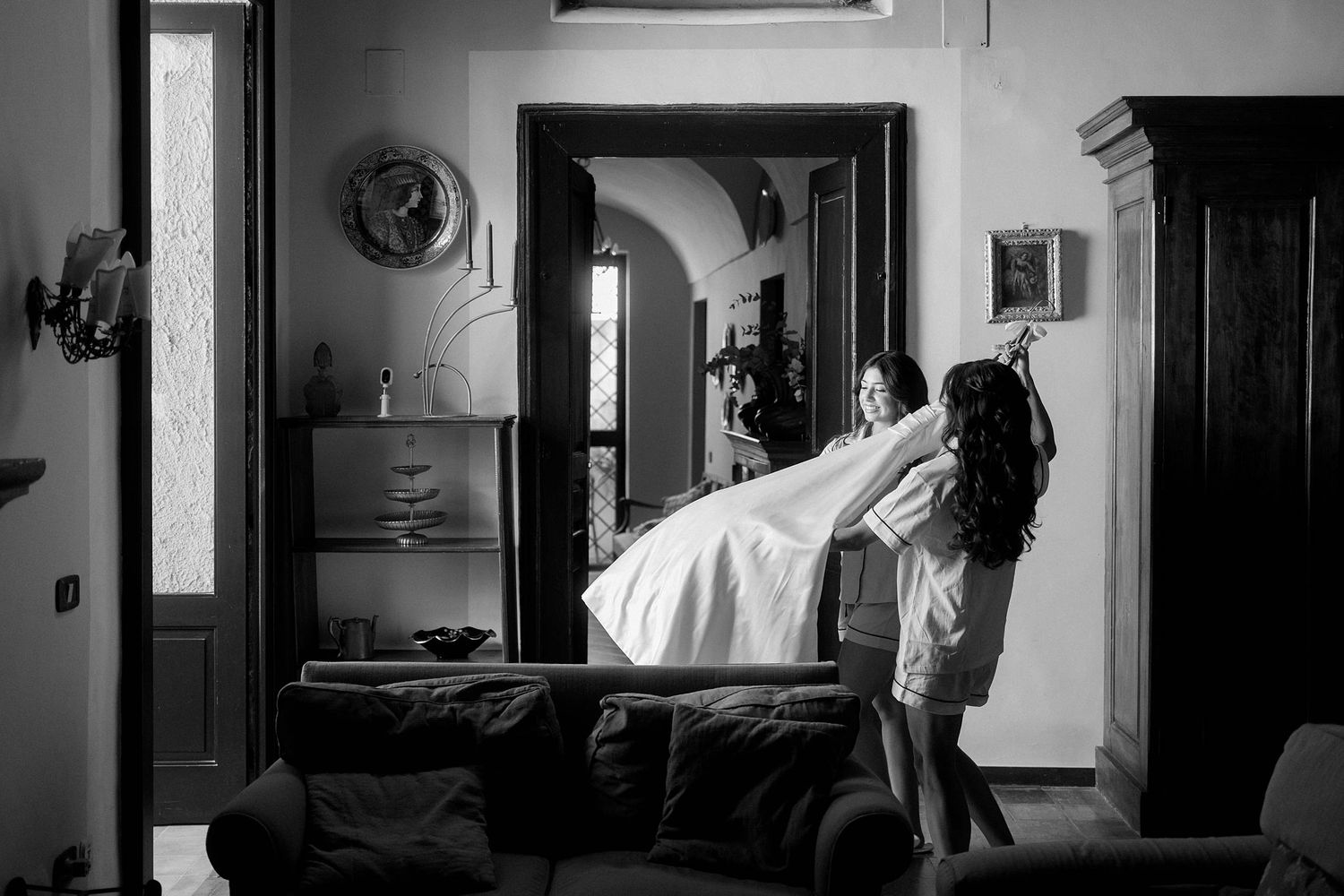 A dramatic black and white photo shows a figure levitating above a couch in a dimly lit living room interior.