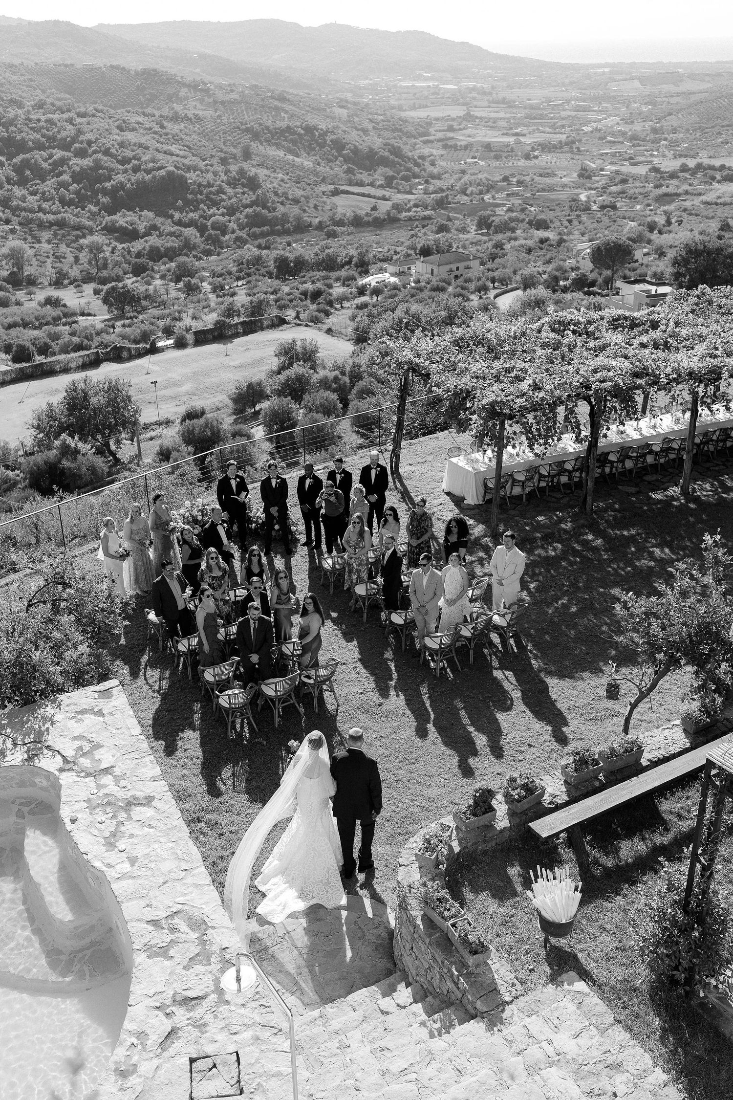 A black and white panoramic sequence showing a group of people walking along a hillside path with scenic valley views.