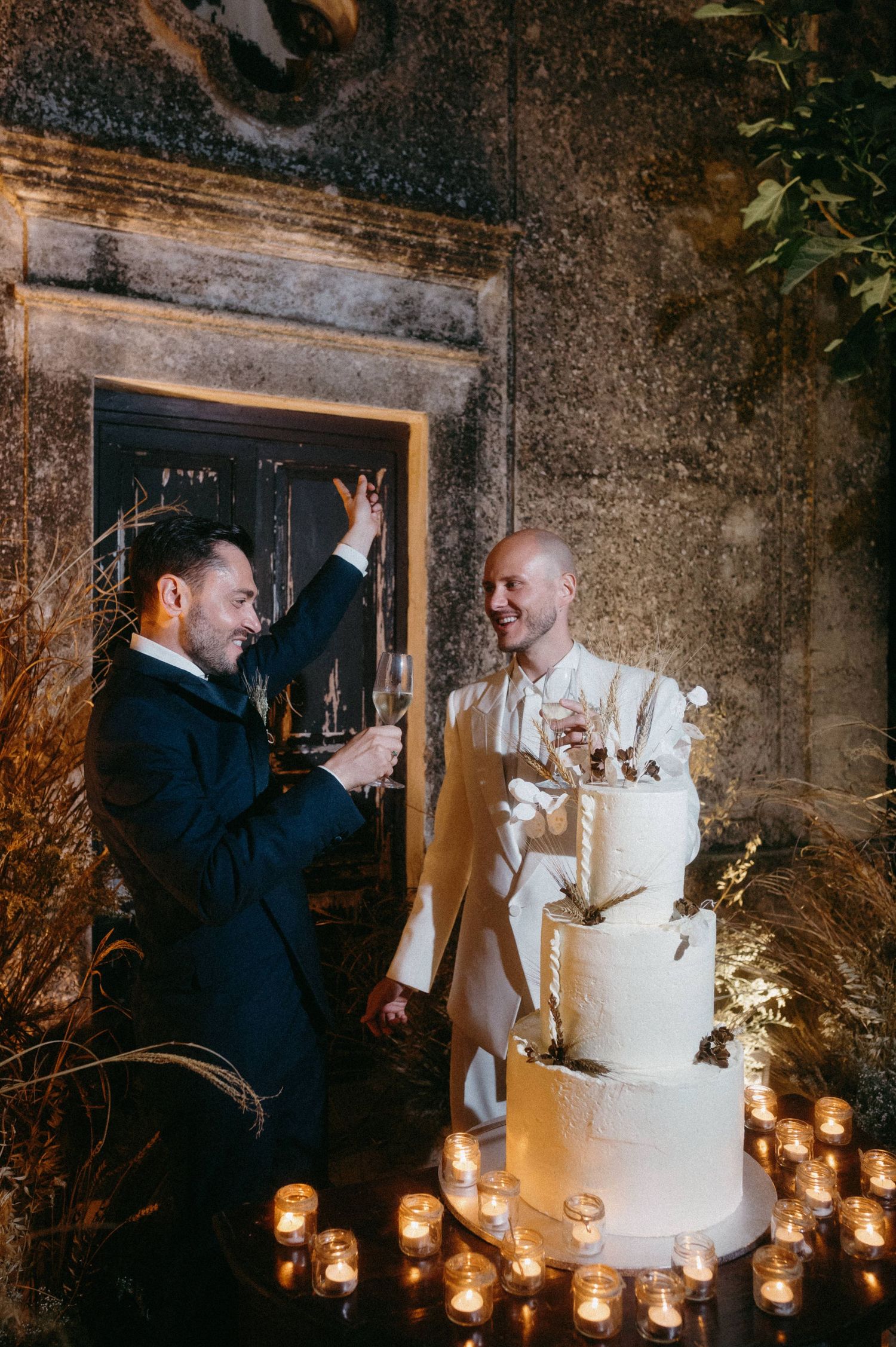 Newlyweds share a joyful moment while cutting their elegant white wedding cake surrounded by candlelight.