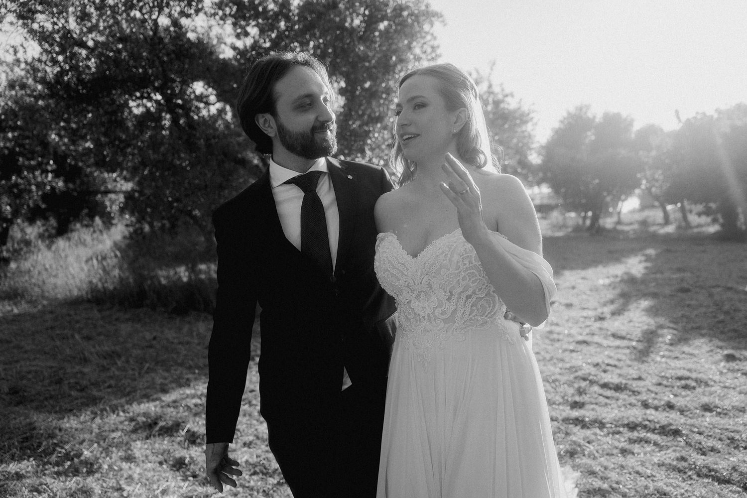 Couple in wedding attire walks together through a sunlit outdoor setting in romantic portraits.