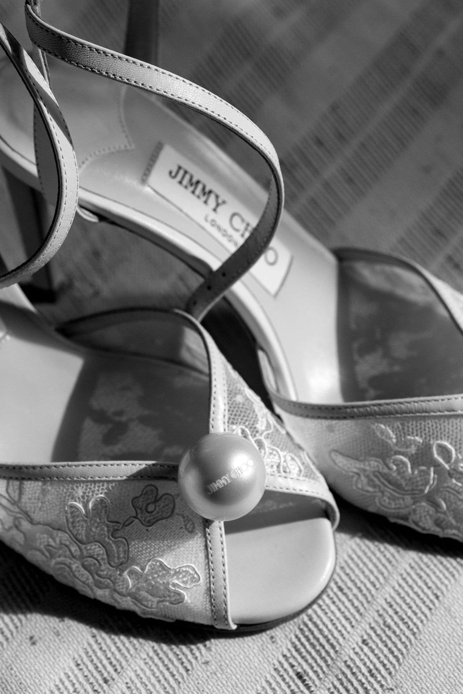 Close-up black and white photo of elegant bridal shoes with floral embroidery details and pearl accents.