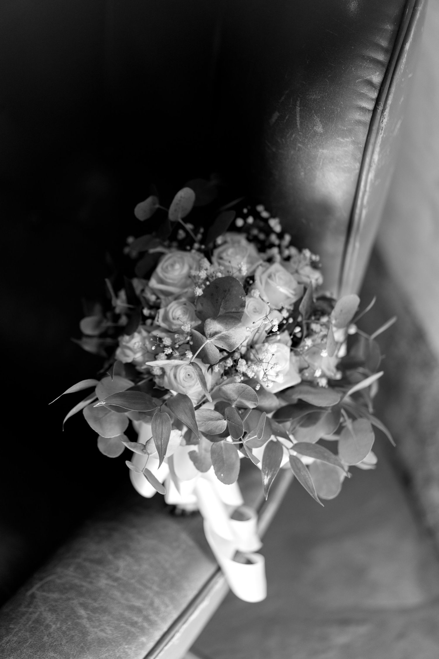 Black and white wedding bouquet with roses and eucalyptus leaves resting on a leather surface.