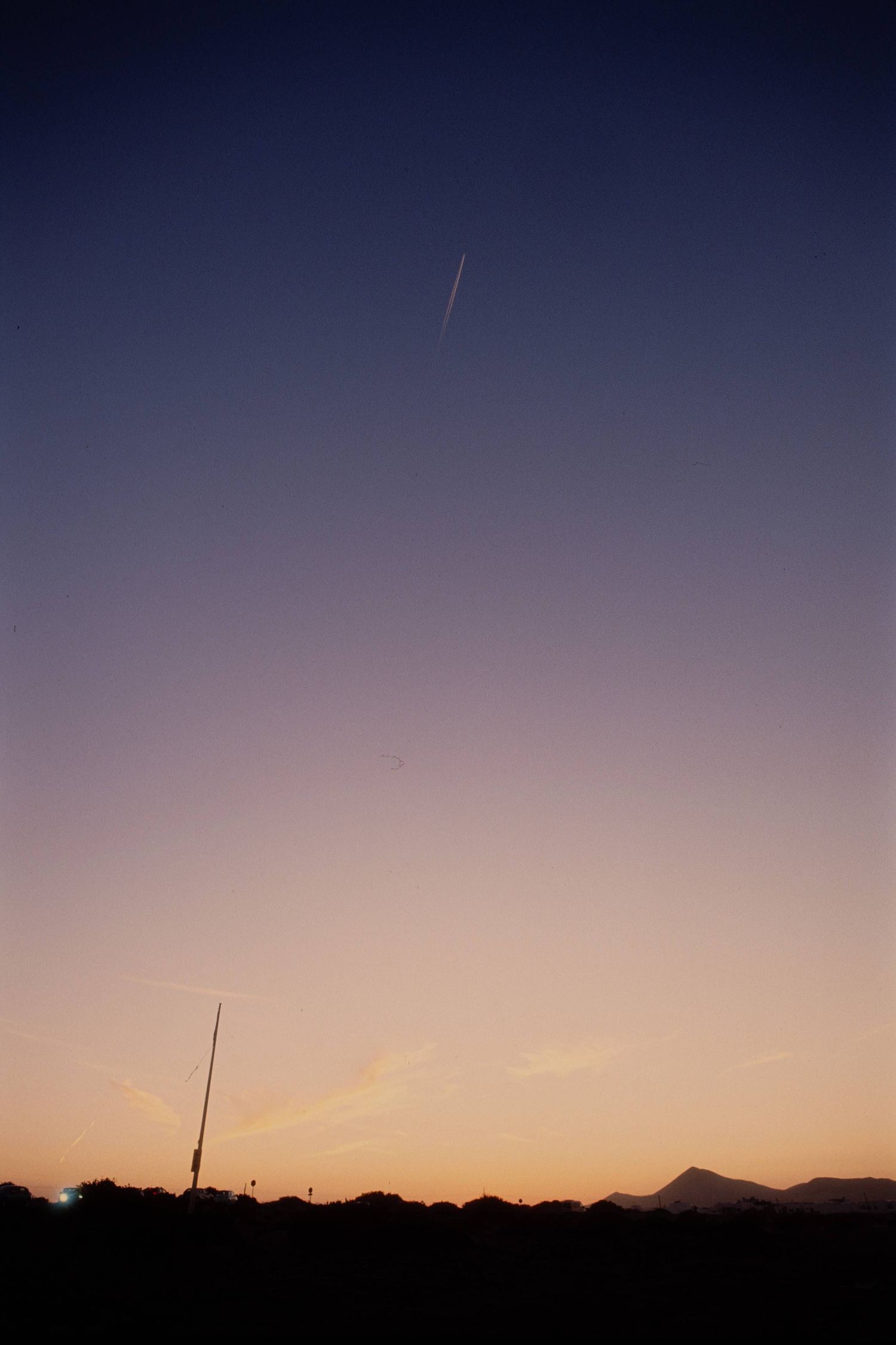 A silhouette of desert mountains against a dusky purple and orange sunset sky with contrails visible above.