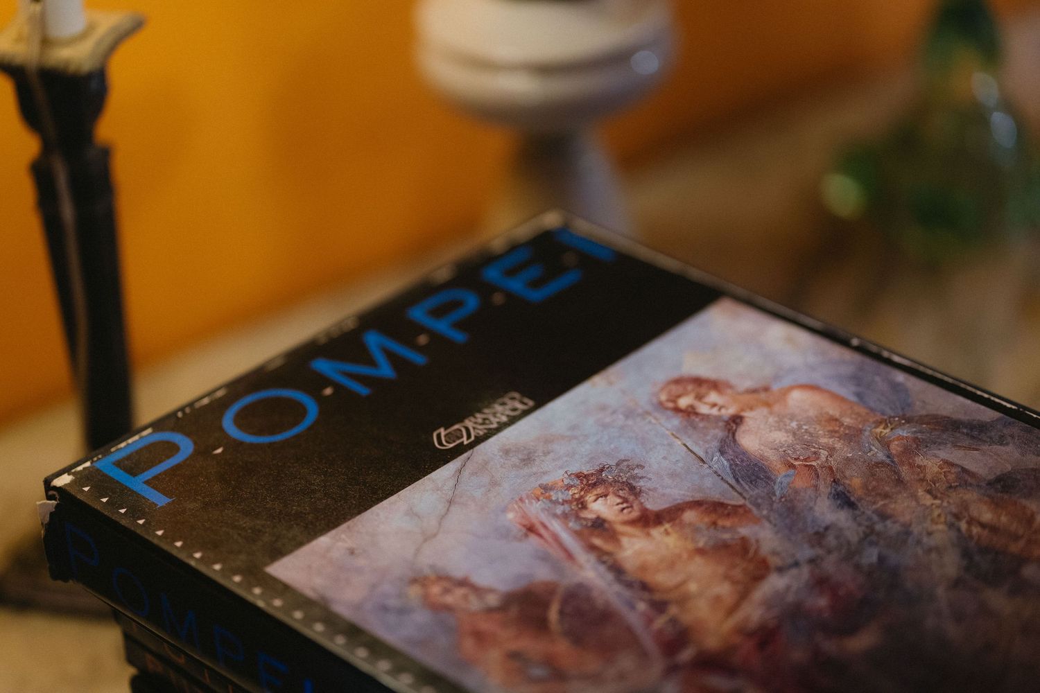 A book titled 'Pompeii' with an ancient fresco artwork on the cover sits on a dark surface.