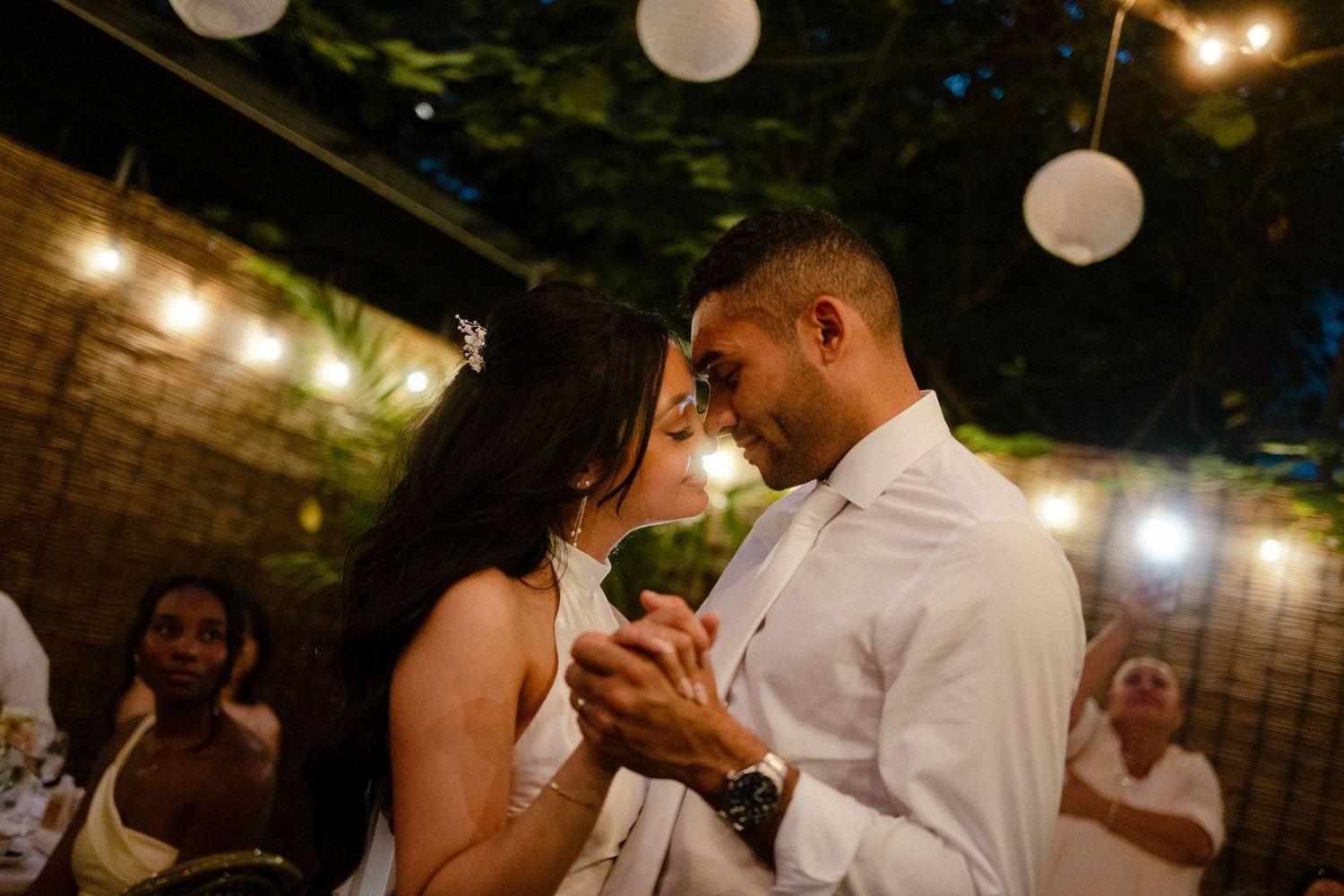 A couple shares their first dance at a wedding reception under glowing paper lanterns and string lights.