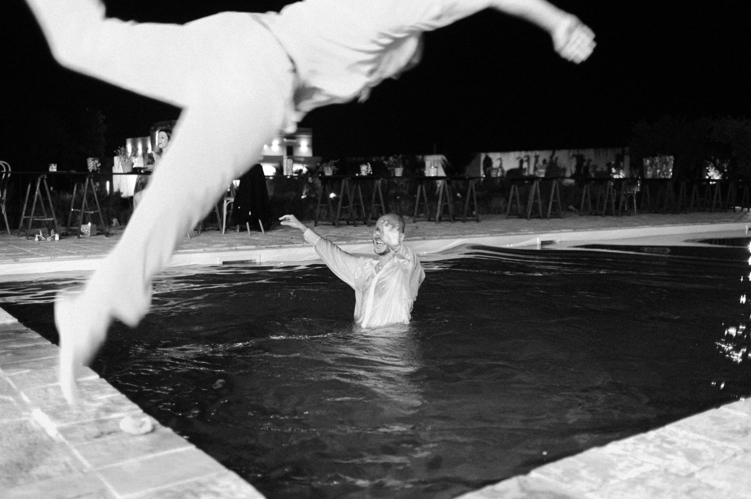 A diver gracefully executes a backflip dive into a dark swimming pool during a nighttime competition event.