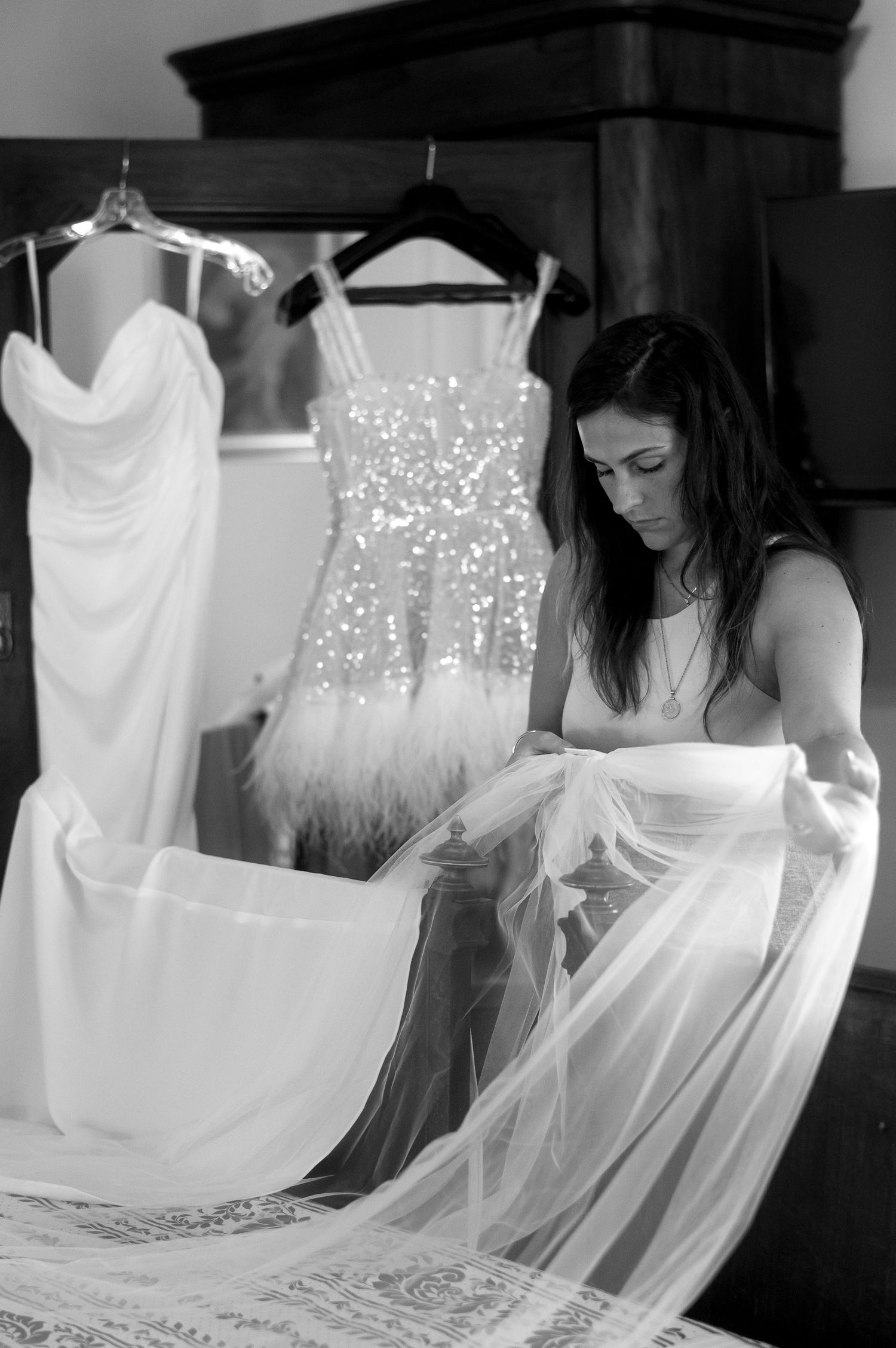 Black and white photo showing wedding dress preparations with a sparkly dress hanging and delicate tulle fabric being handled.