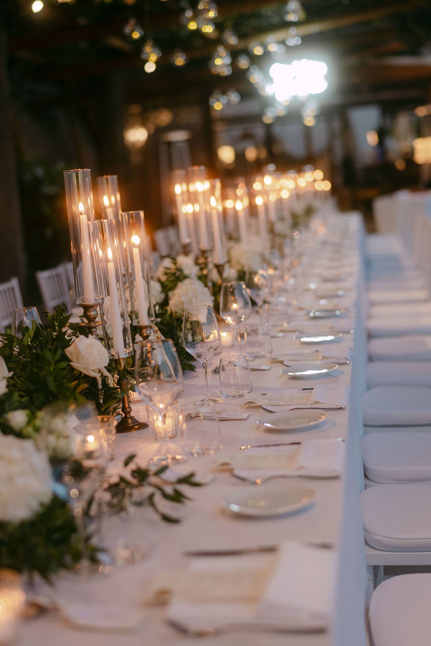 Elegant wedding reception table settings with white linens, candles, and floral arrangements creating a romantic atmosphere.