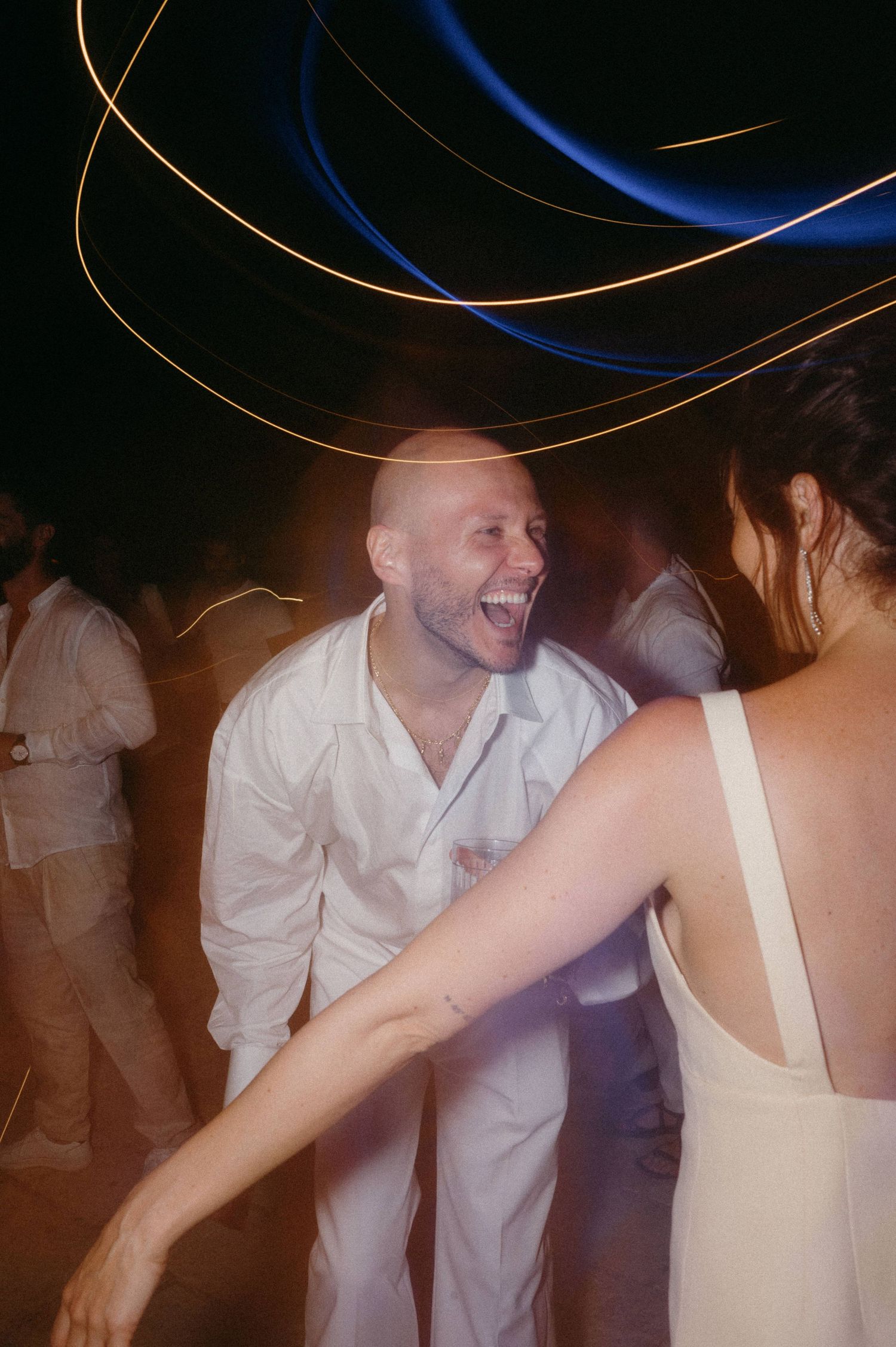 People dancing and celebrating at a wedding reception with light trails and motion blur creating a dynamic atmosphere.