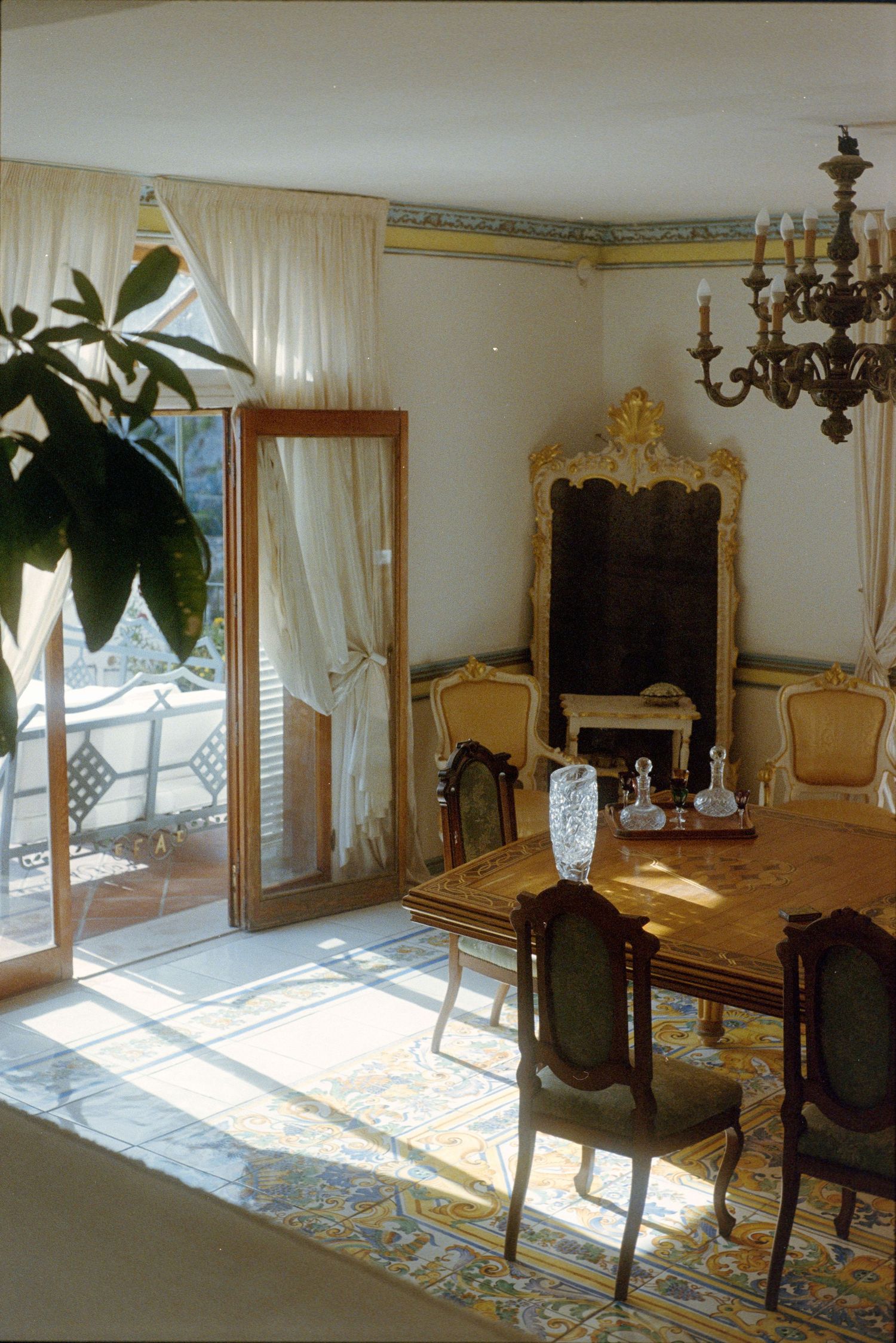 Elegant French provincial dining room with ornate chairs, gilded mirrors, and sheer white curtains letting in natural light.