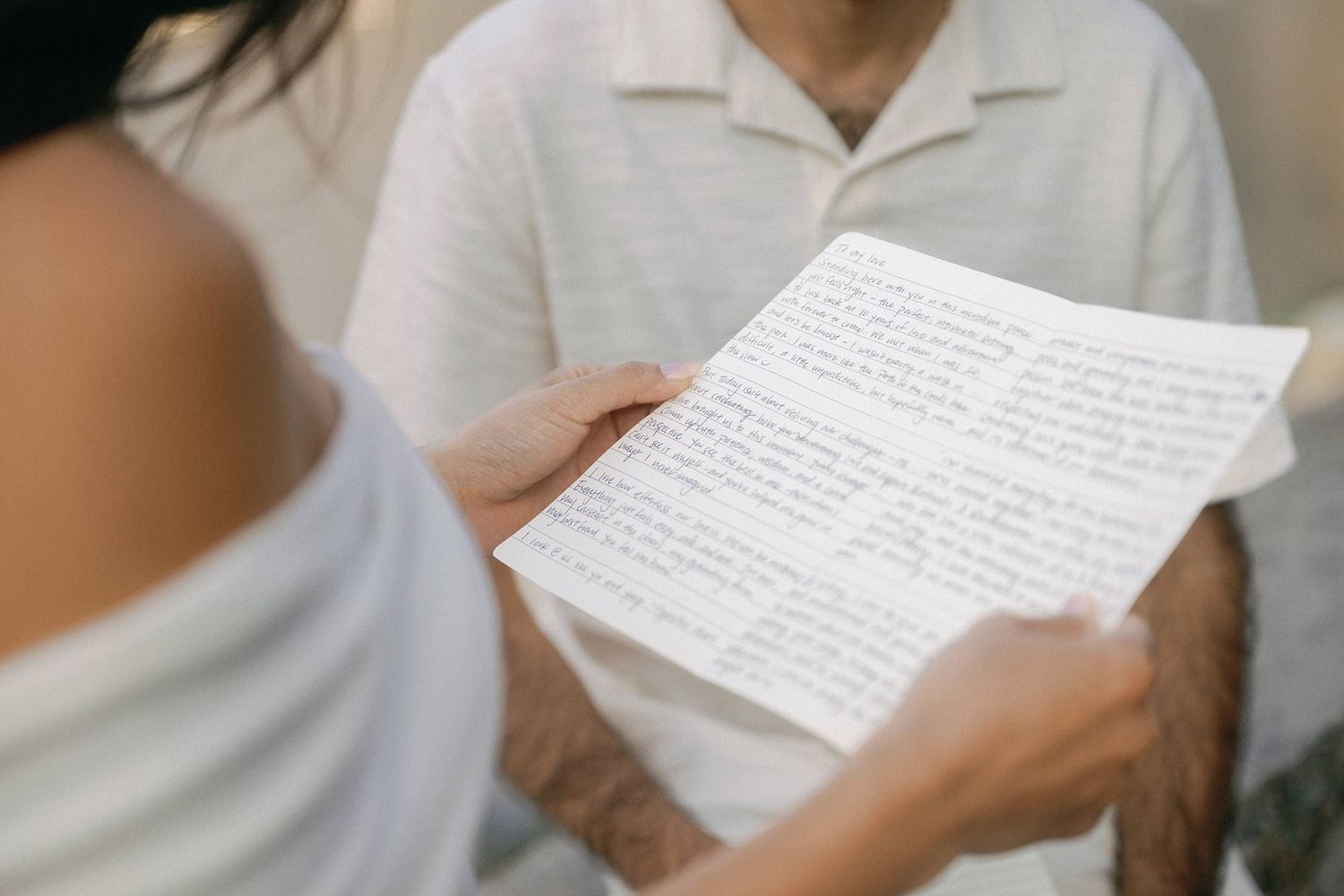 A person in white clothing holds a handwritten letter or document, reading its contents carefully.