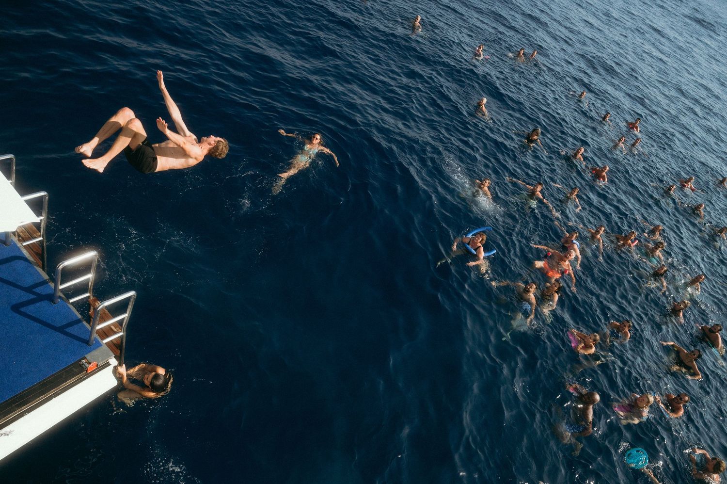 Divers swim in deep blue ocean waters near a boat platform on a sunny day at sea.