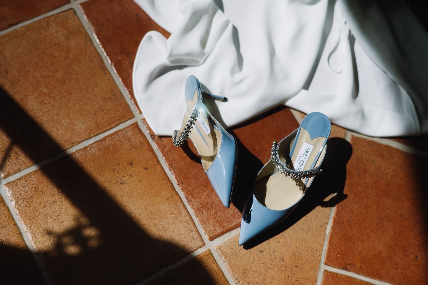 Light blue vintage heels with white socks rest on terracotta tiles, casting dramatic shadows in sunlight.