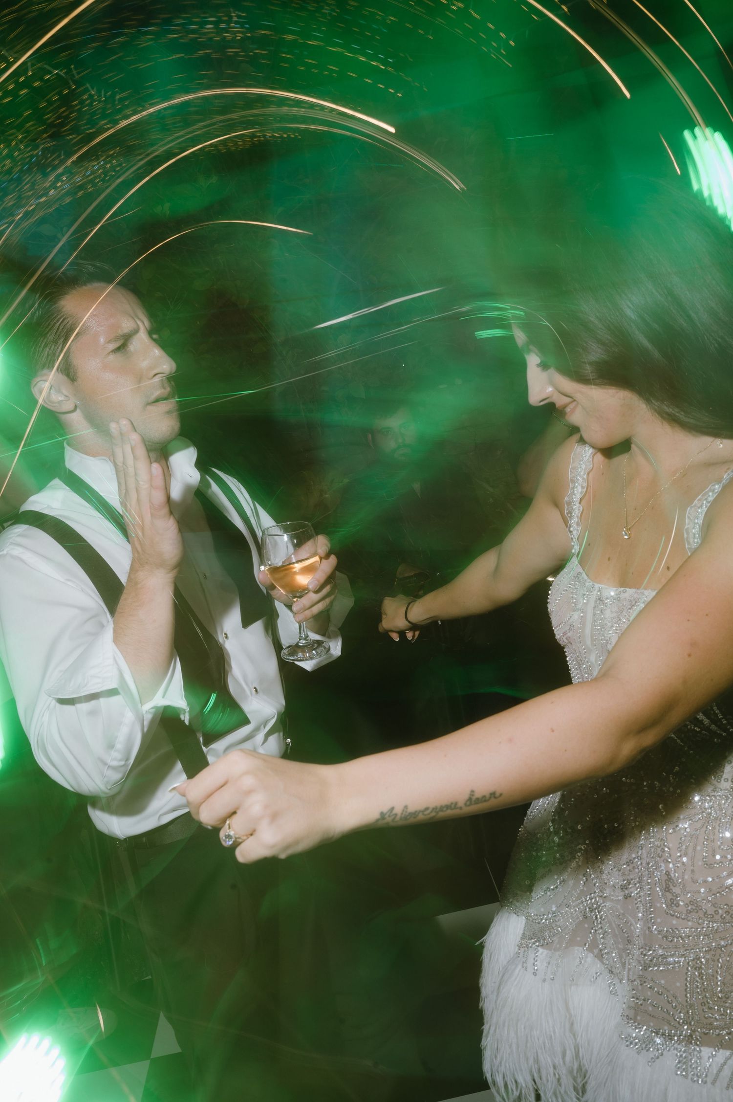 Motion blur captures people dancing and drinking at a party with dramatic green lighting effects in the background.
