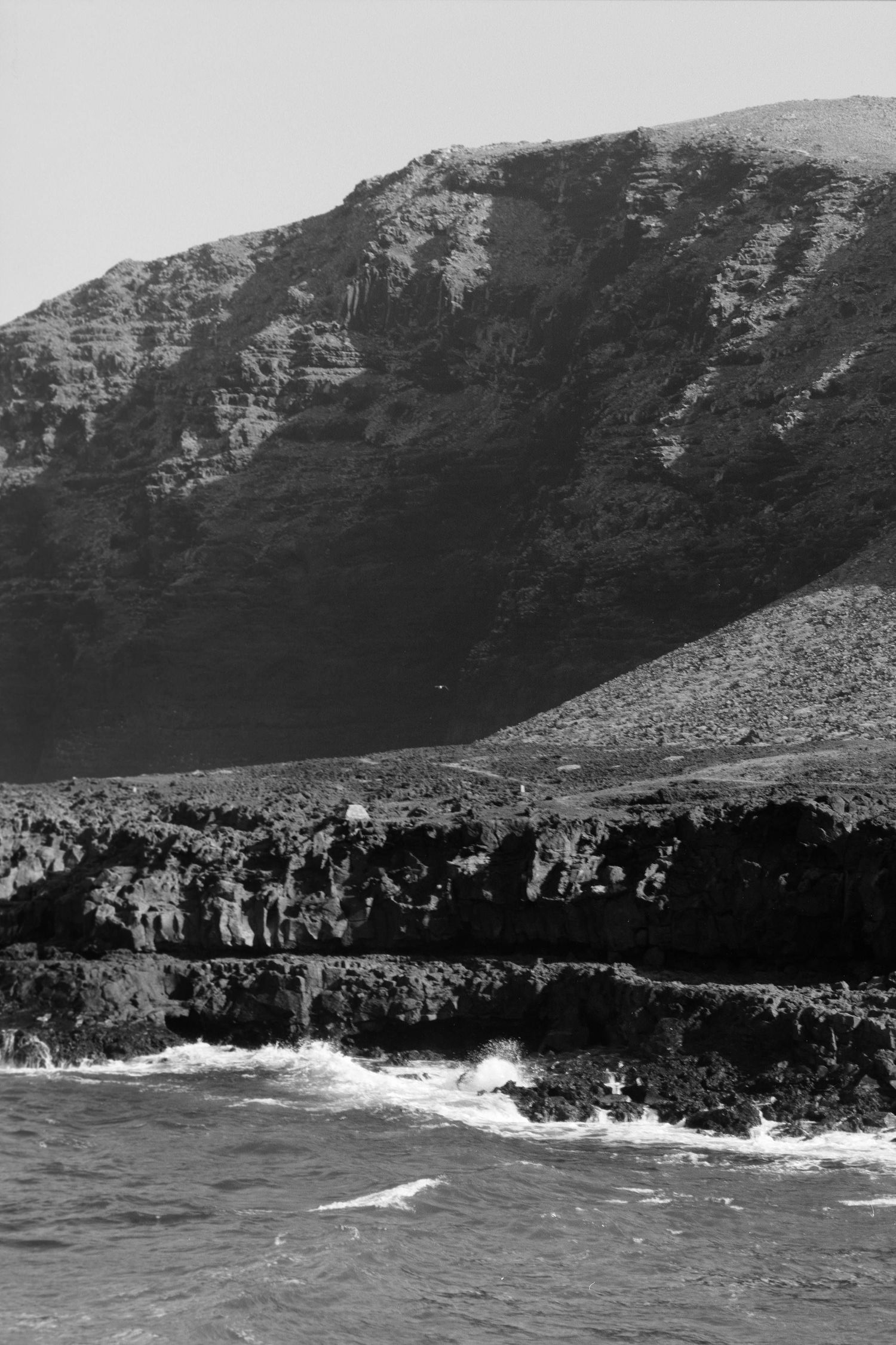 A dramatic black and white coastal landscape shows rugged cliffs meeting crashing waves against rocky shores.
