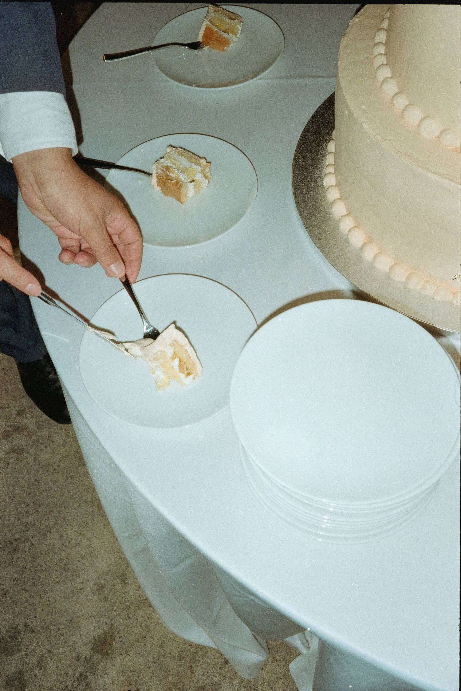 Step by step process of cutting and serving a white wedding cake on white plates.