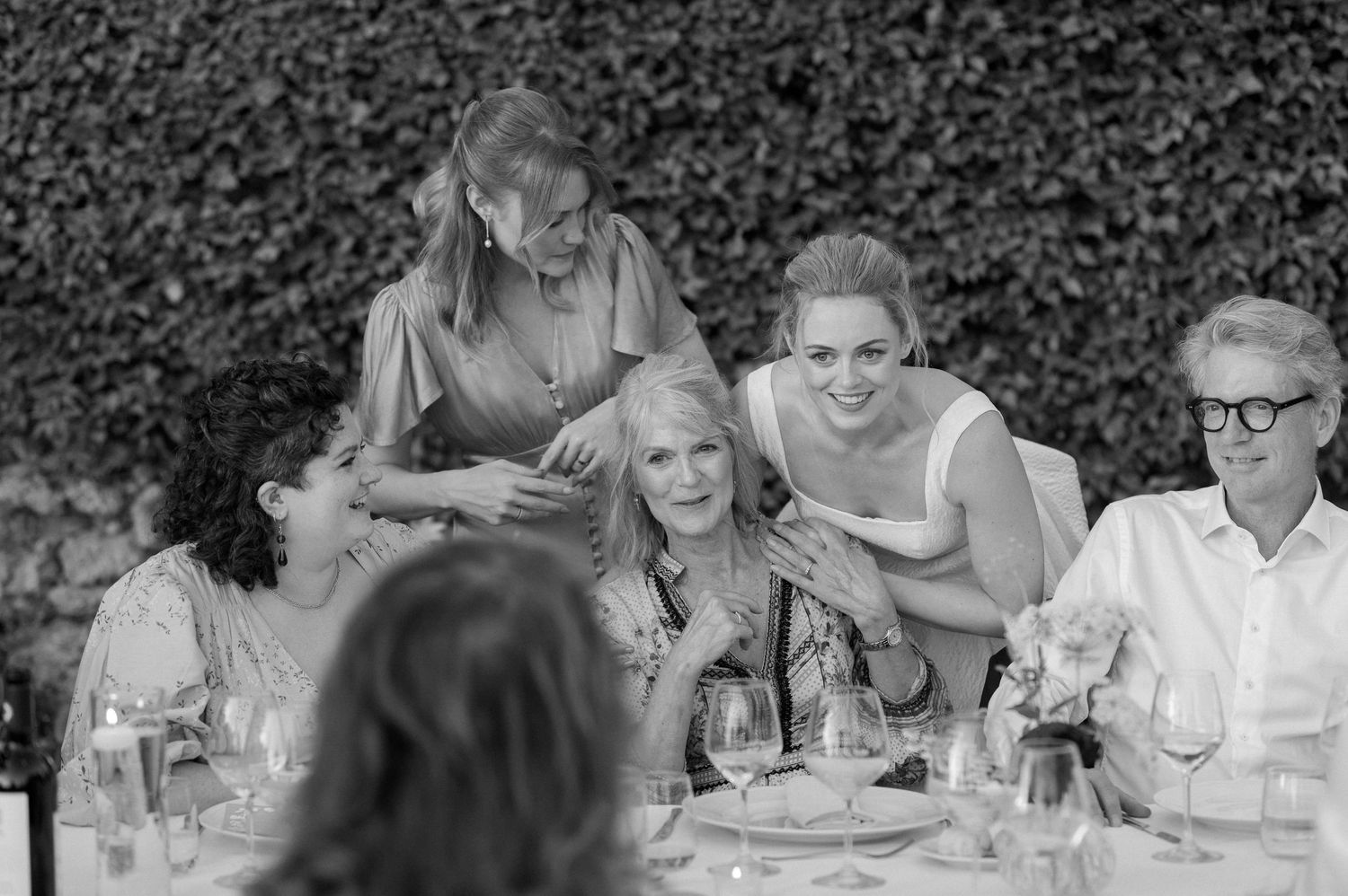 Black and white photo of guests enjoying an outdoor wedding reception at long tables in a garden setting.