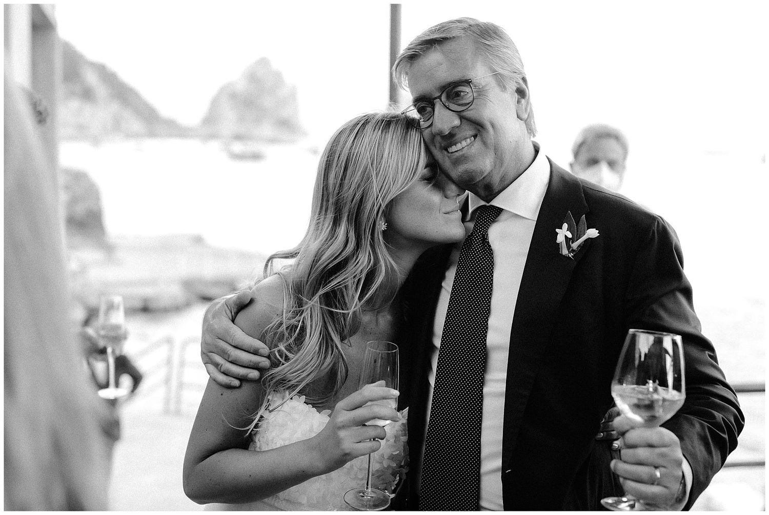 A touching black and white moment at a wedding reception as two people share an embrace while holding wine glasses.