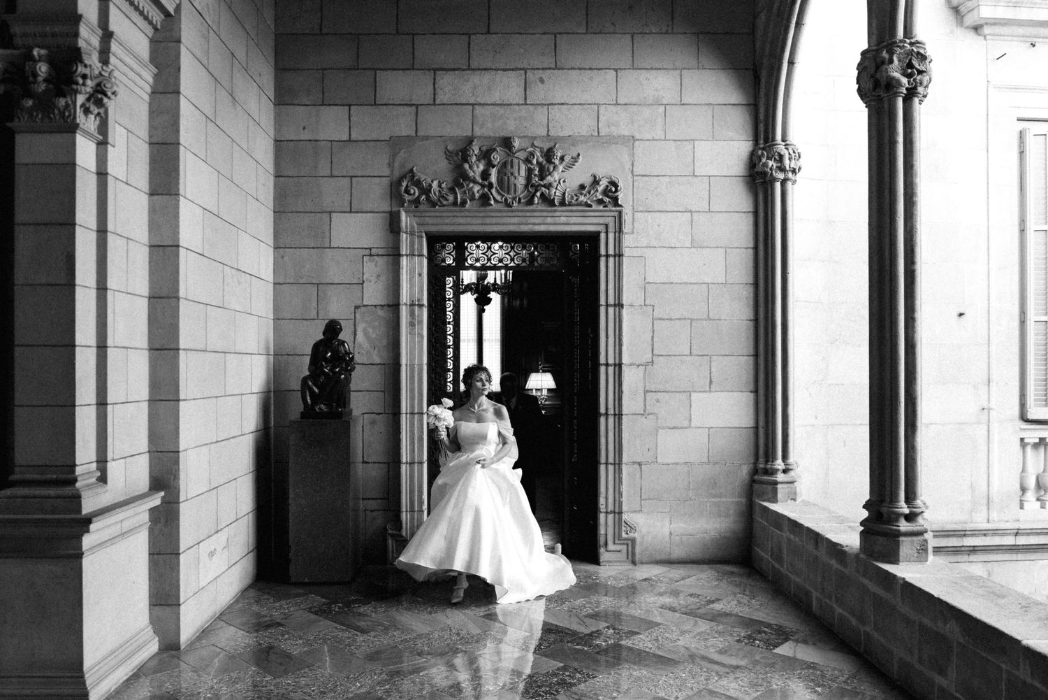 A black and white photograph of a couple entering through an ornate doorway in a stone hallway.