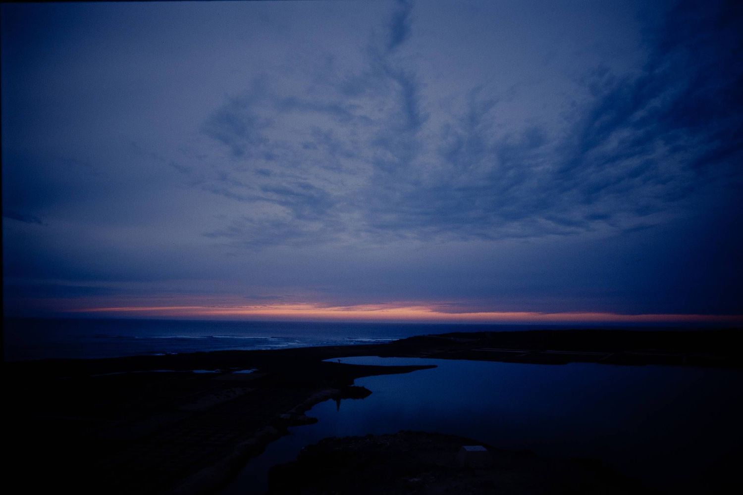 Dramatic twilight sky with dark clouds reflects on calm water during sunset over a tranquil landscape.
