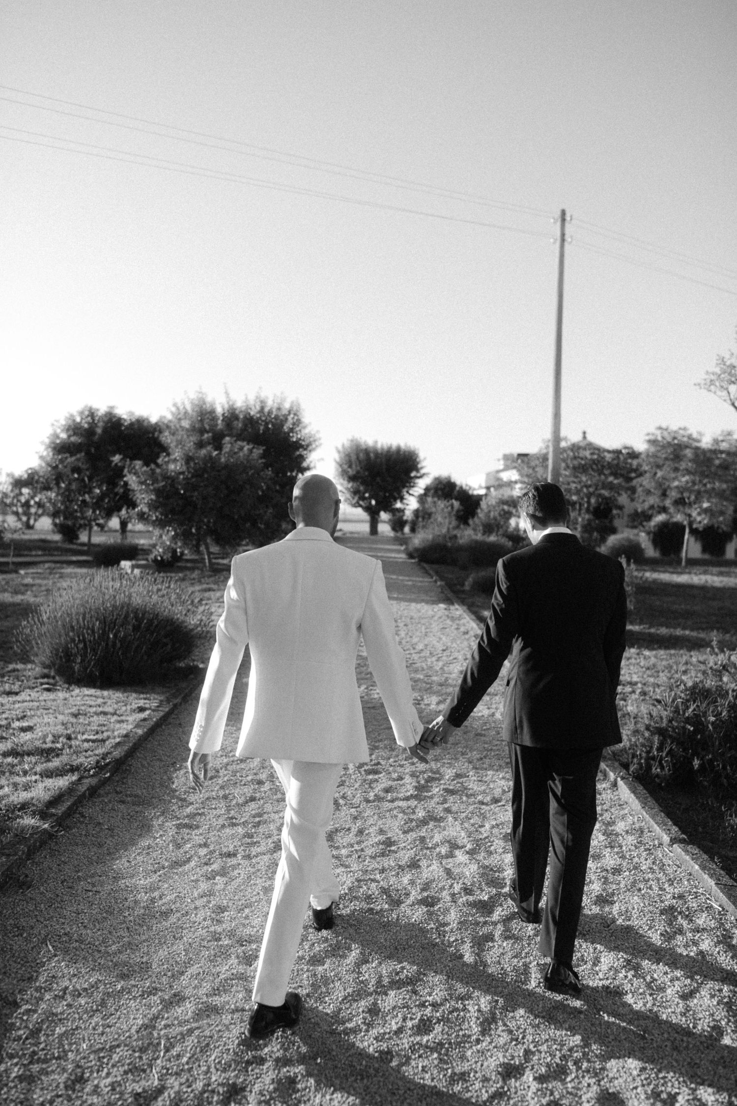 Two figures in contrasting black and white attire walk together through a rural field in a black and white photograph.