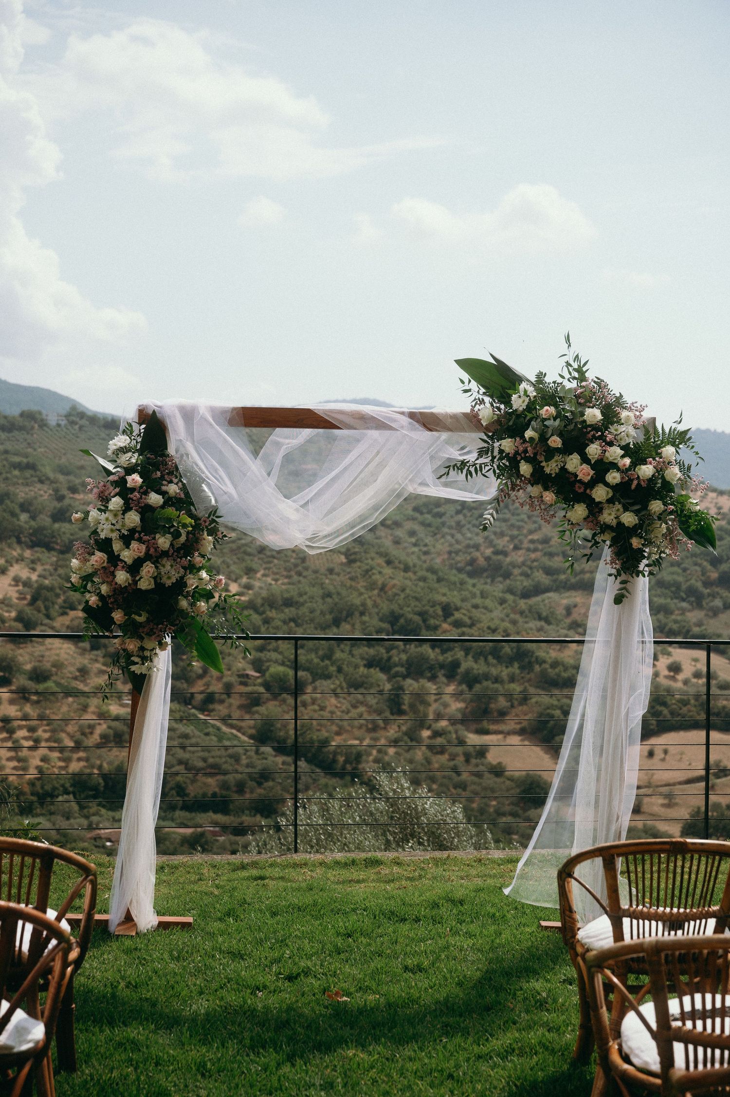 Elegant outdoor wedding arch with white fabric draping and floral arrangements set against a scenic mountain backdrop.