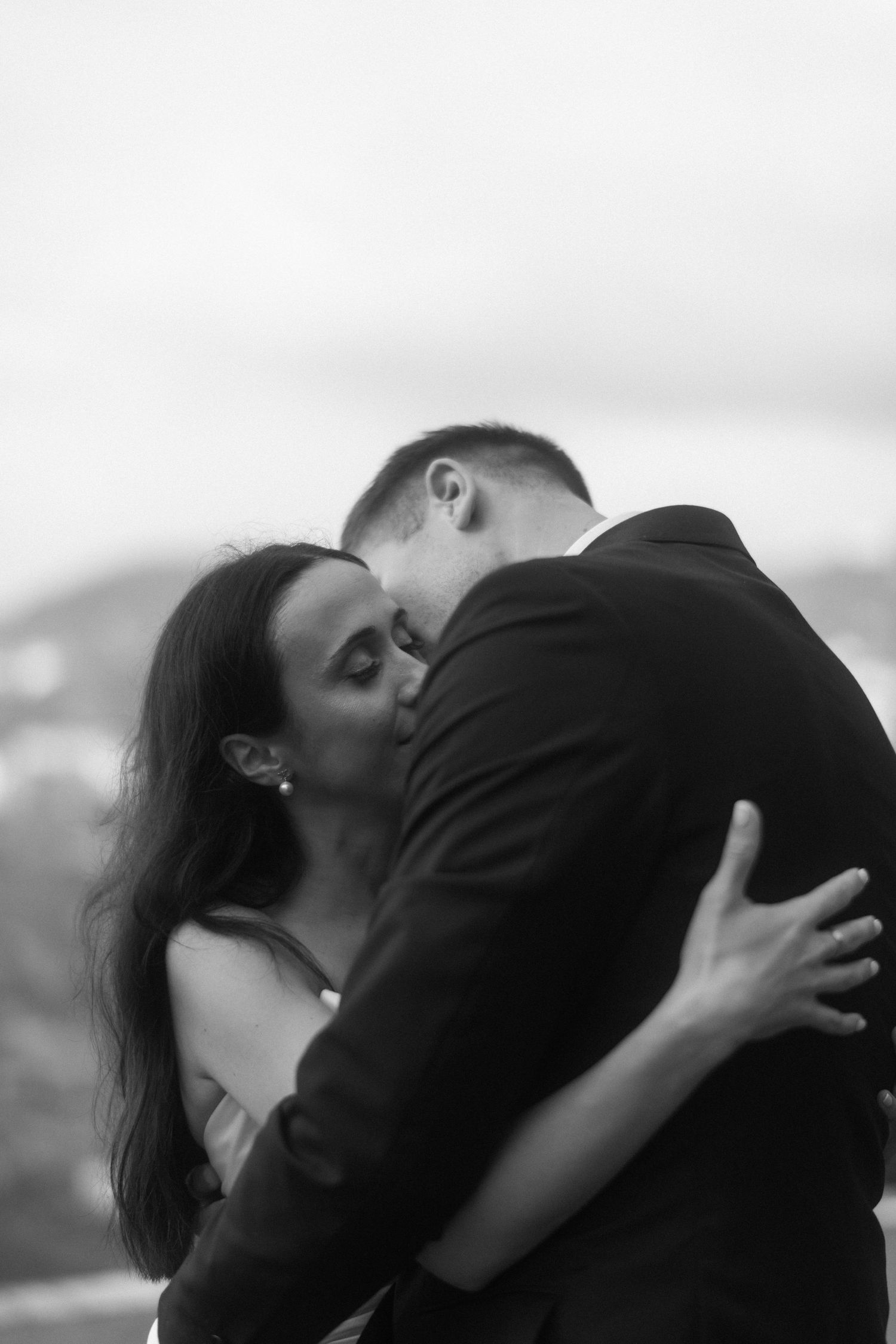 Intimate black and white photograph of a couple sharing a tender embrace against a minimalist background.