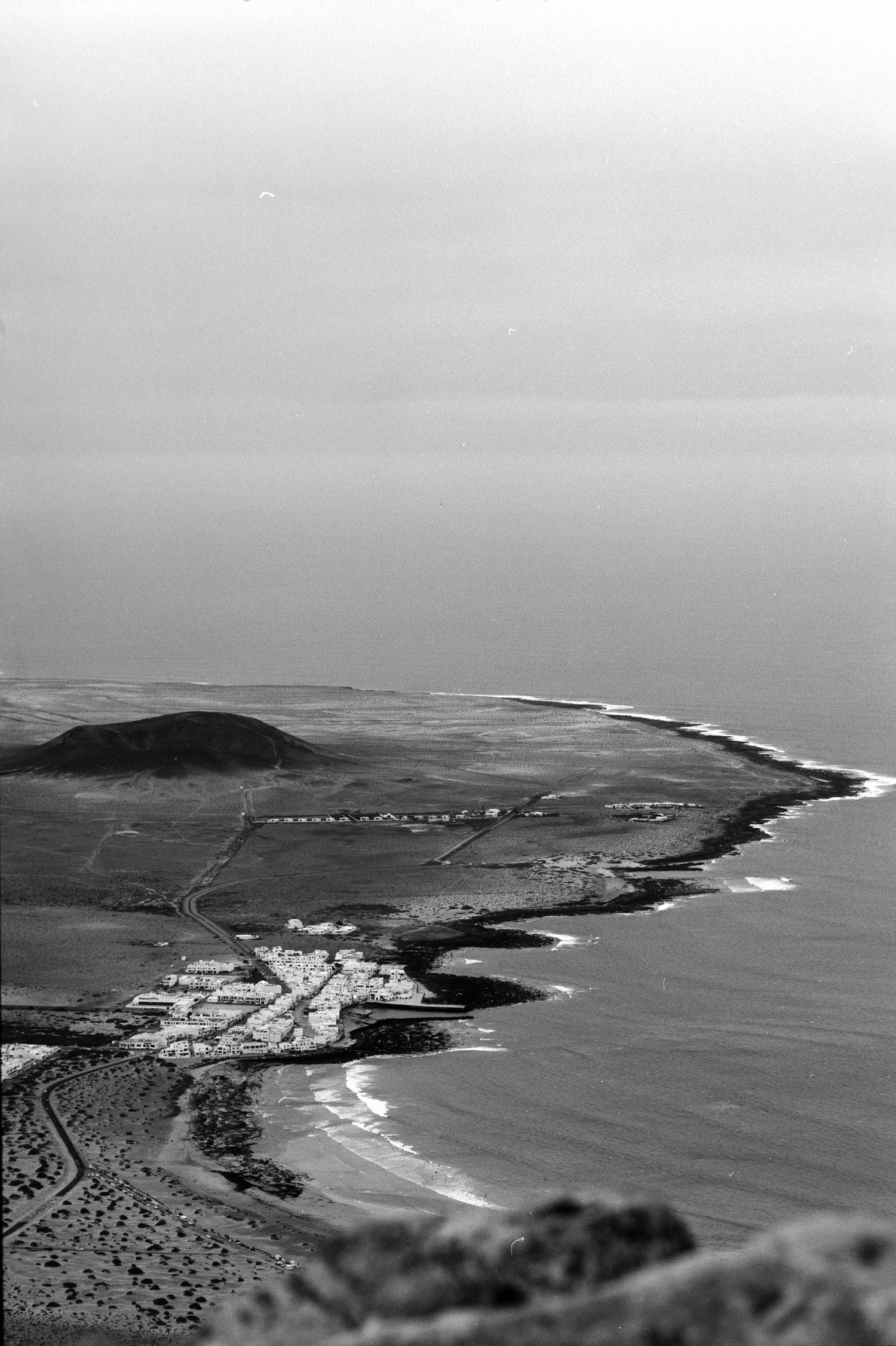 Aerial black and white view of a coastal shoreline with a small town nestled along the curving beach.