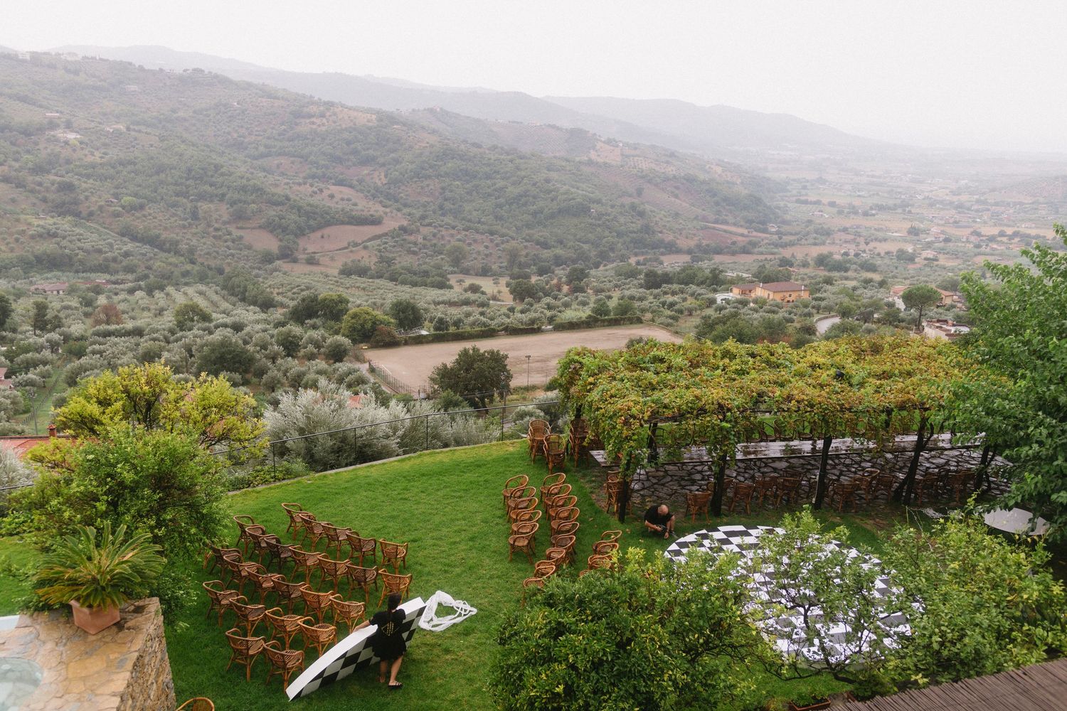 Panoramic mountain landscape view with rolling hills, lush greenery, and scattered buildings in the distance.