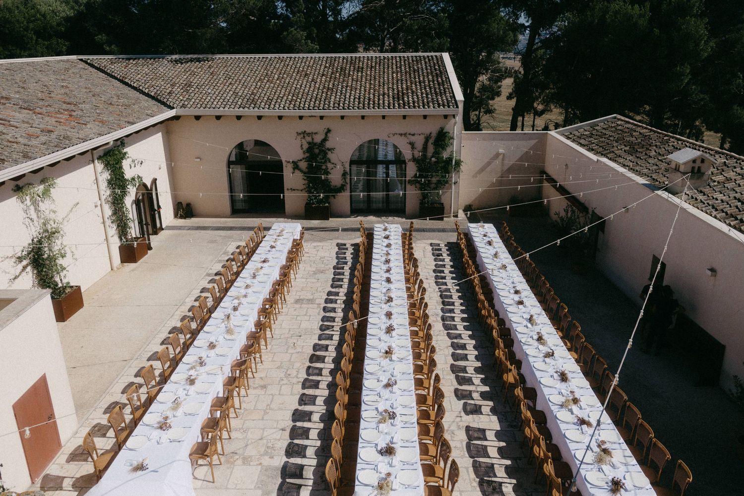 Long rows of wooden chairs arranged under string lights create an elegant outdoor wedding ceremony setup.