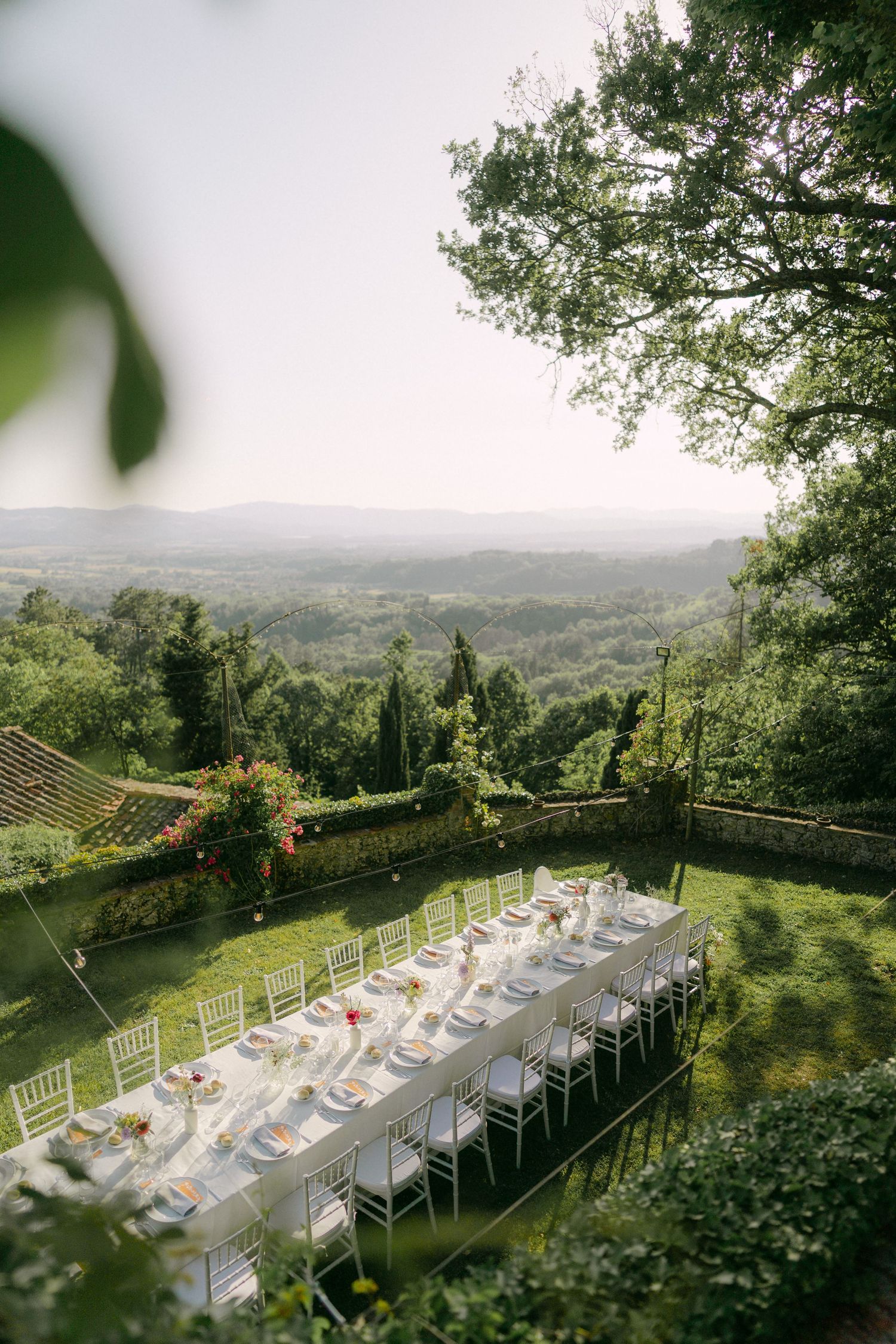 Panoramic view of an elegant outdoor wedding reception setup with white chairs and tables overlooking a lush hillside landscape.
