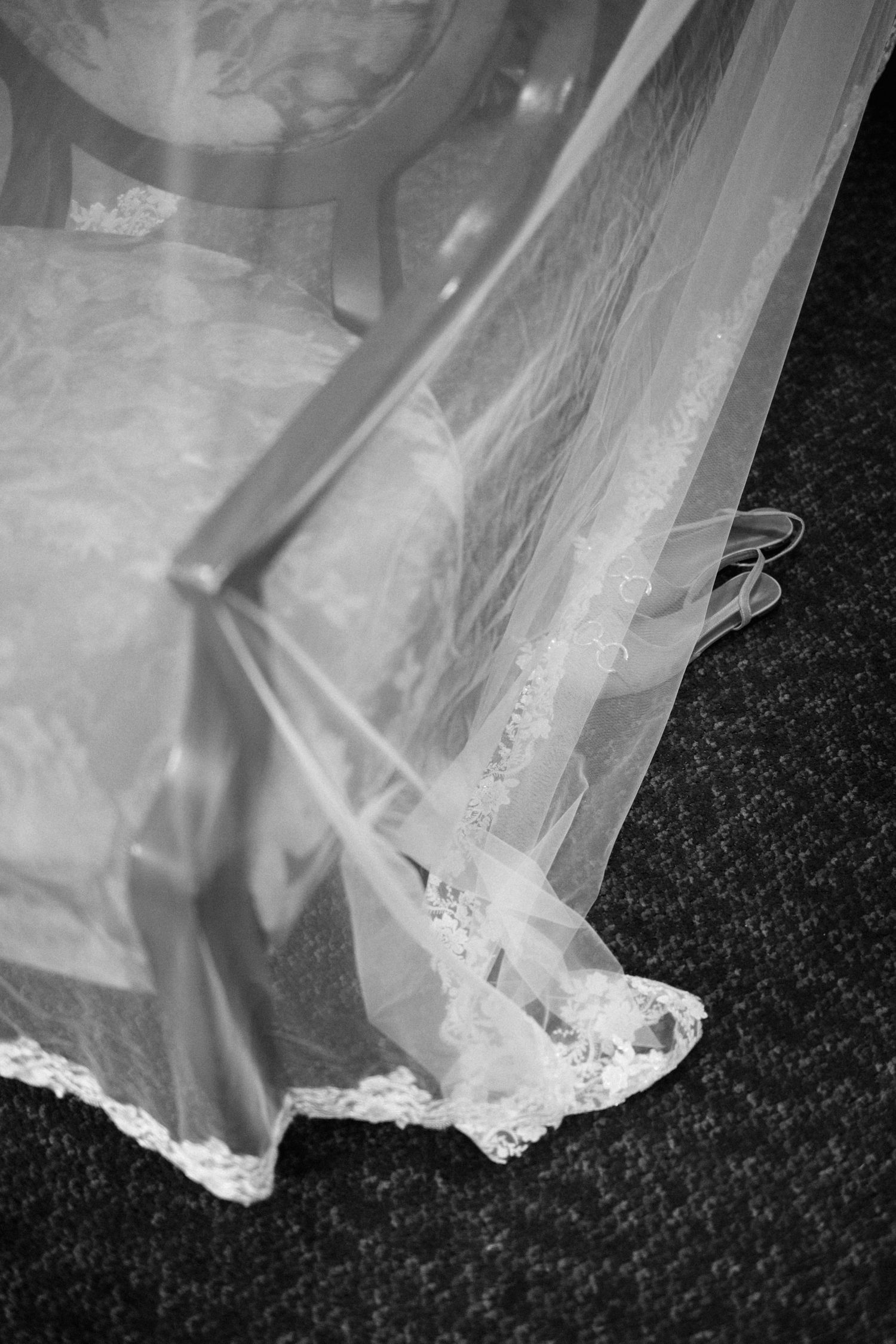 A delicate white wedding dress veil with lace trim detail lies draped against a dark carpet background.