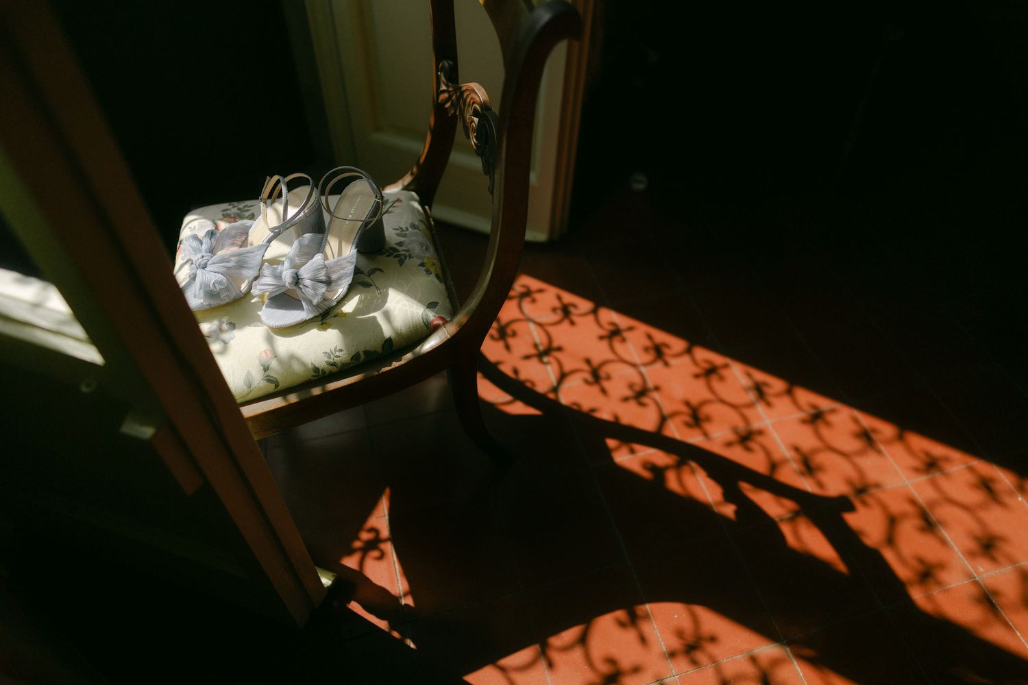 Sunlight casts geometric shadows through window blinds onto floor beside crumpled newspaper.
