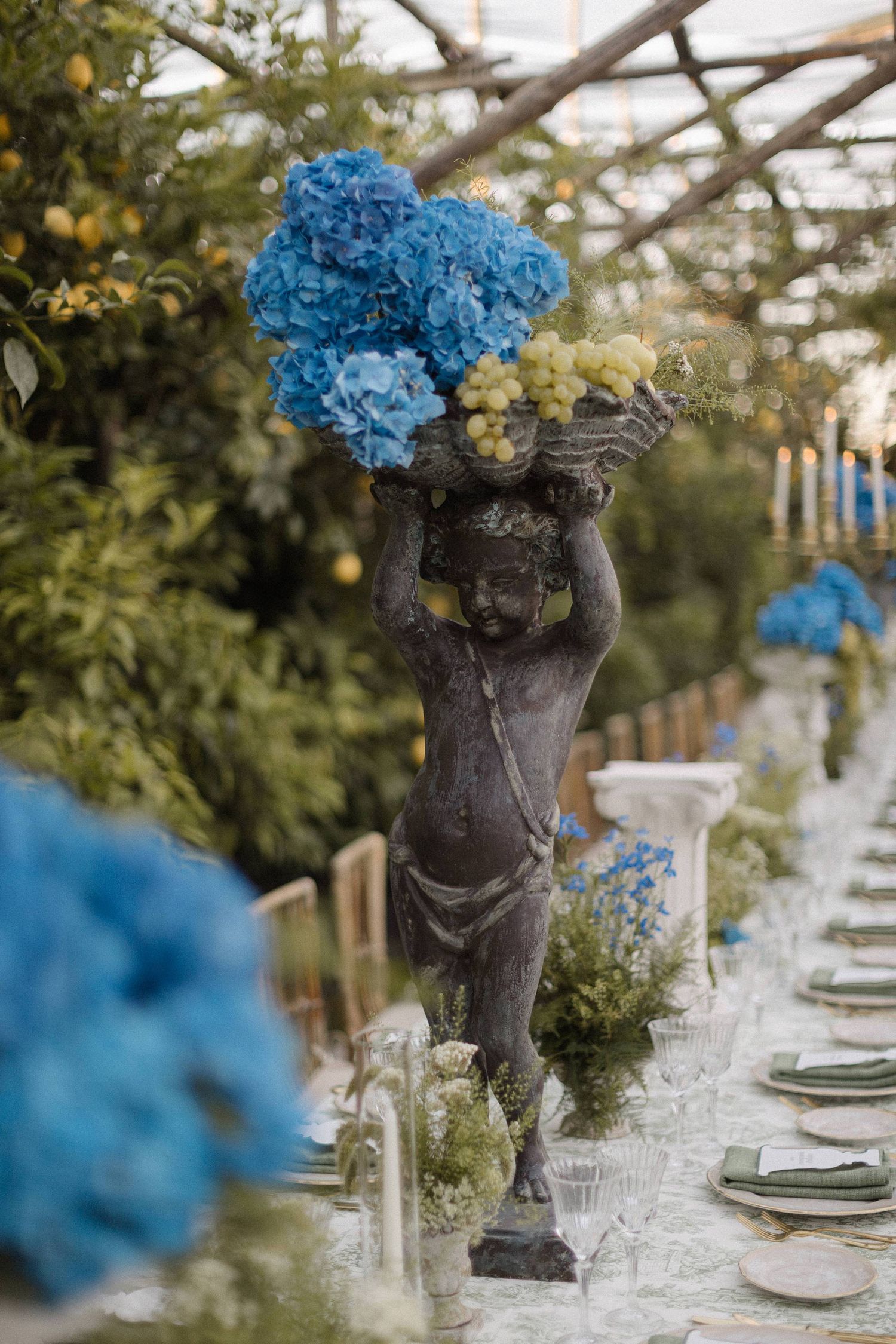 Bronze cherub statue centerpiece holding blue hydrangeas at an elegant outdoor wedding reception table.