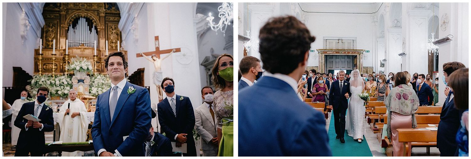 A groom stands at the altar in a blue suit inside an ornate church as guests look on during a wedding ceremony.