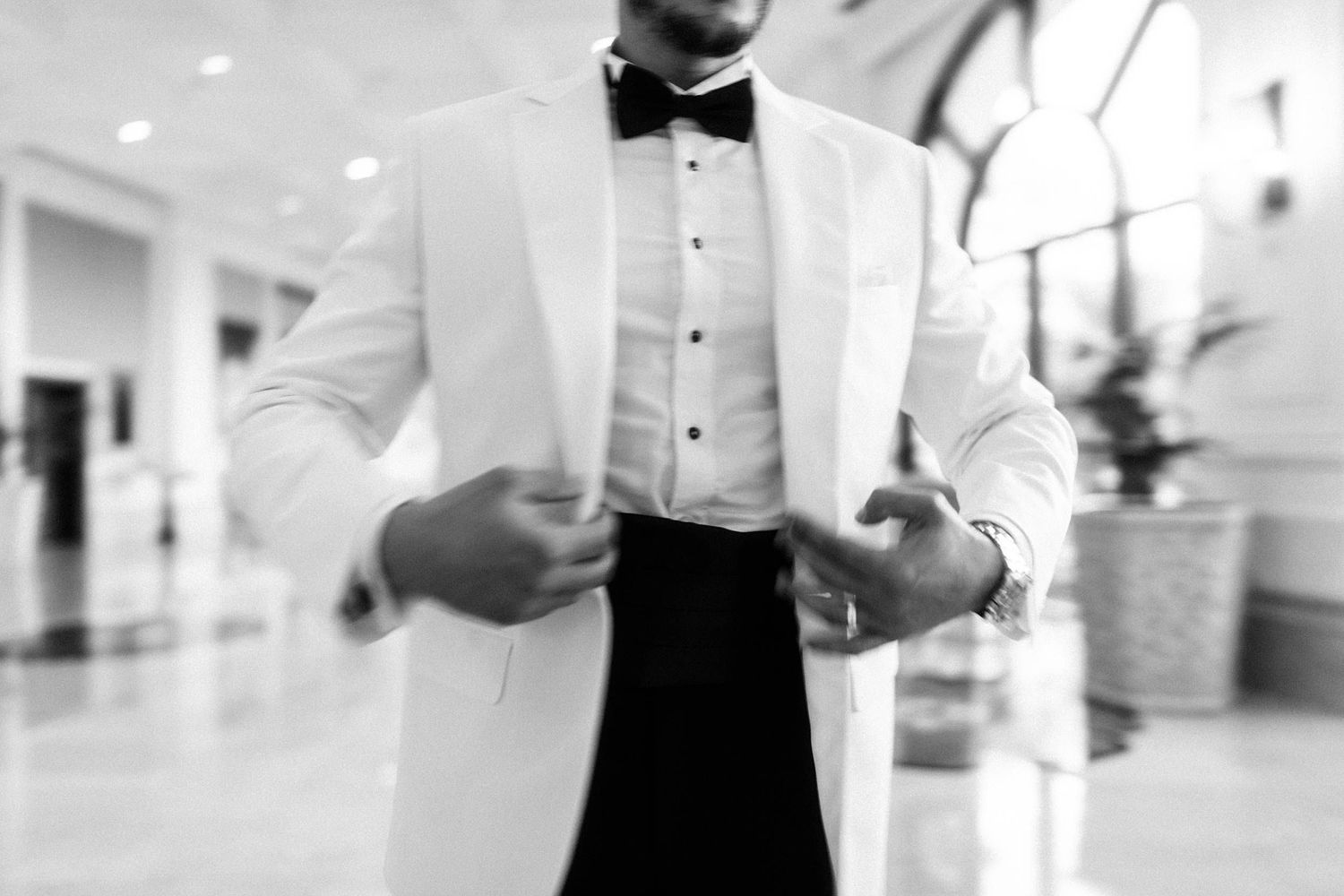 Elegant black and white photo showing a crisp white dinner jacket with bow tie and formal attire in a bright hallway.