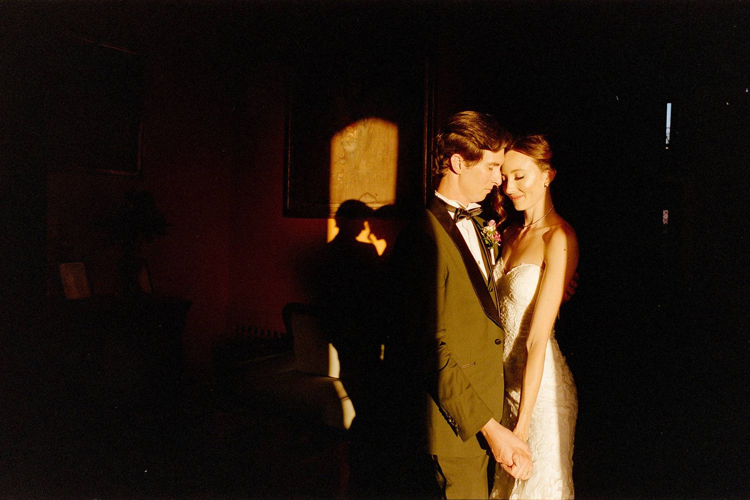 A couple shares a romantic dance together in a dimly lit room during what appears to be a wedding celebration.