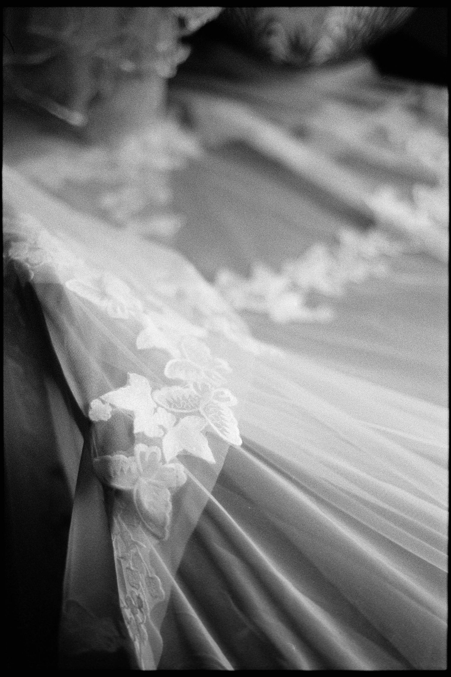 Close-up black and white detail of delicate lace and tulle fabric on a wedding dress.