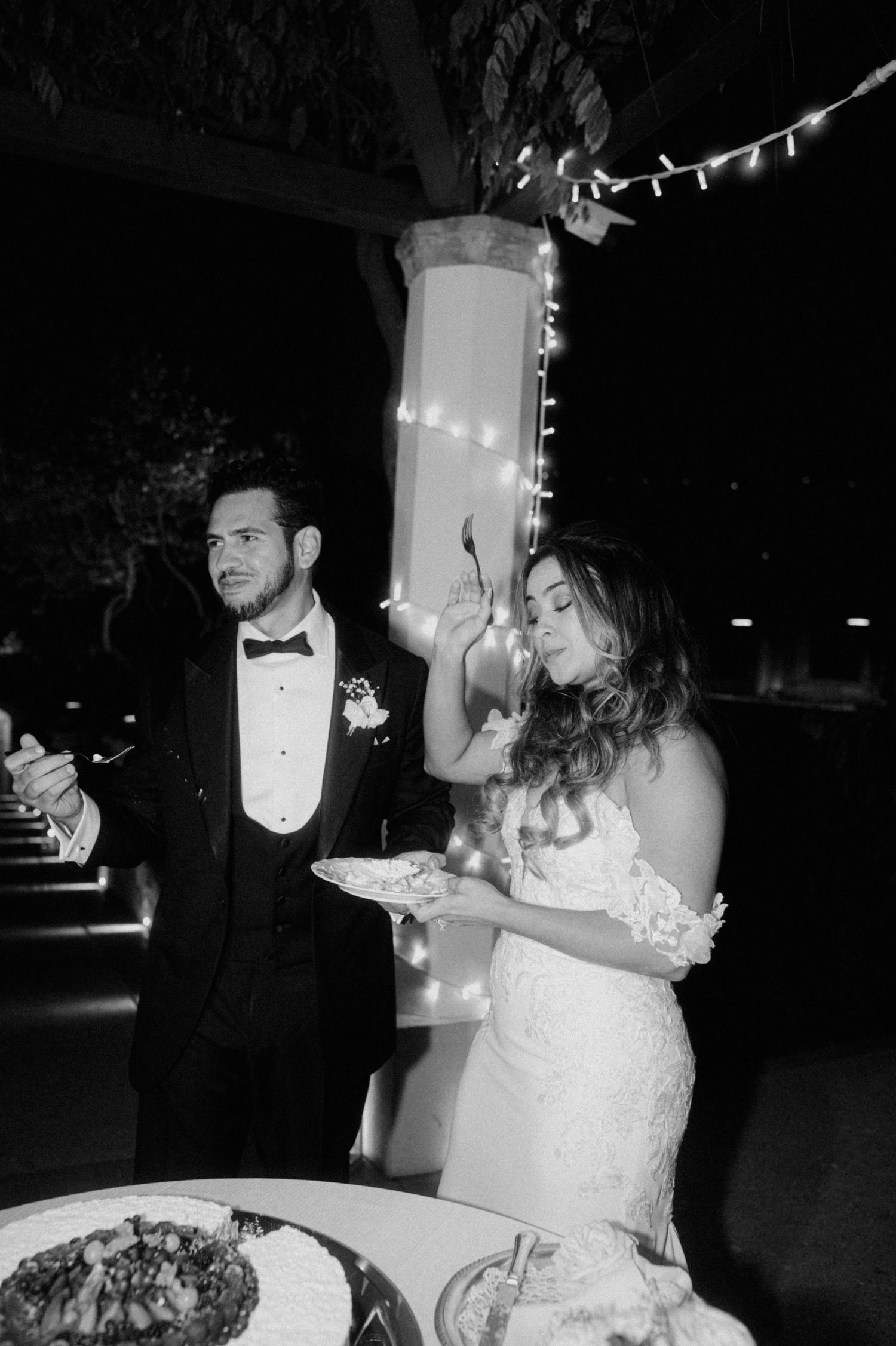 A couple shares their first dance at a wedding reception while guests look on in black and white photography.