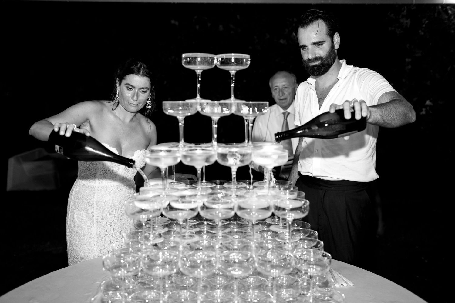 A bartender carefully stacks delicate champagne glasses into a tower formation at a dimly lit bar.