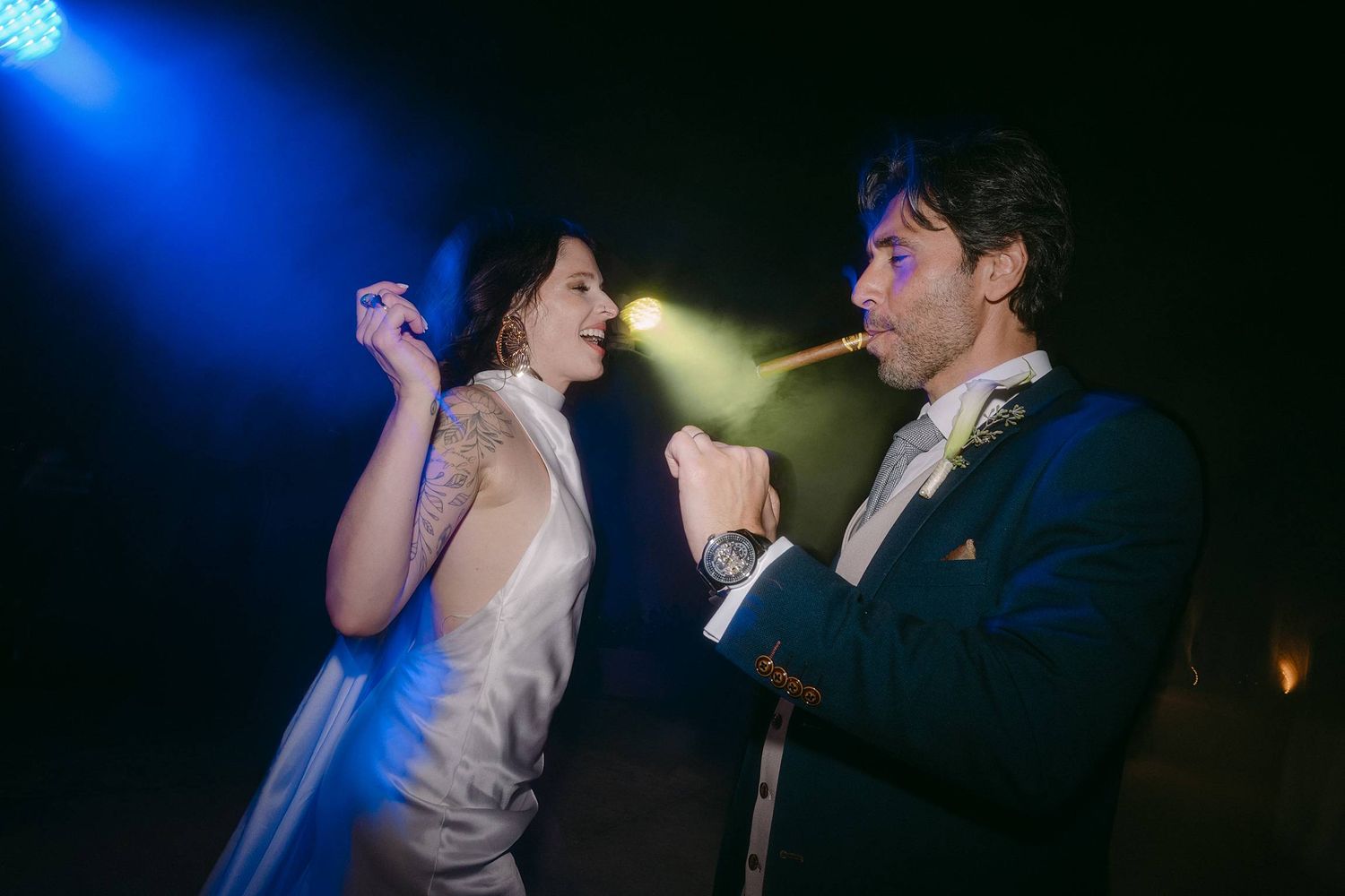 A couple shares a romantic moment on the dance floor under blue and yellow spotlights at an evening celebration.